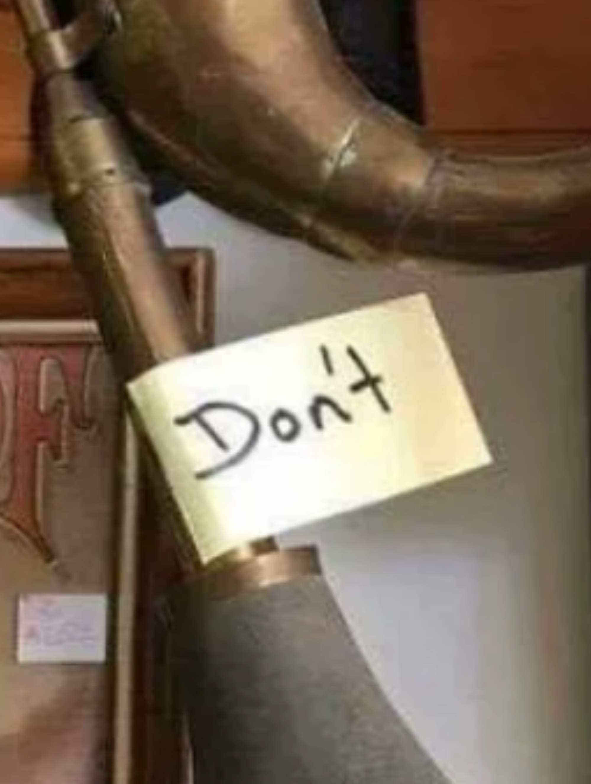 Antique horn with a "Don’t" note attached, hanging on a wooden beam amidst vintage items, suggesting the horn is not to be used