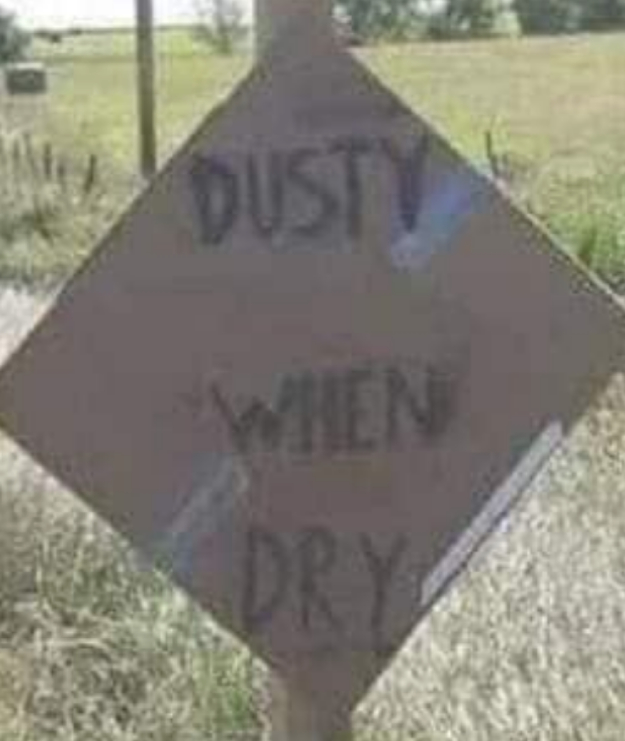 Road sign on a rural road reads "Muddy When Wet" and "Dusty When Dry," highlighting varying conditions based on weather