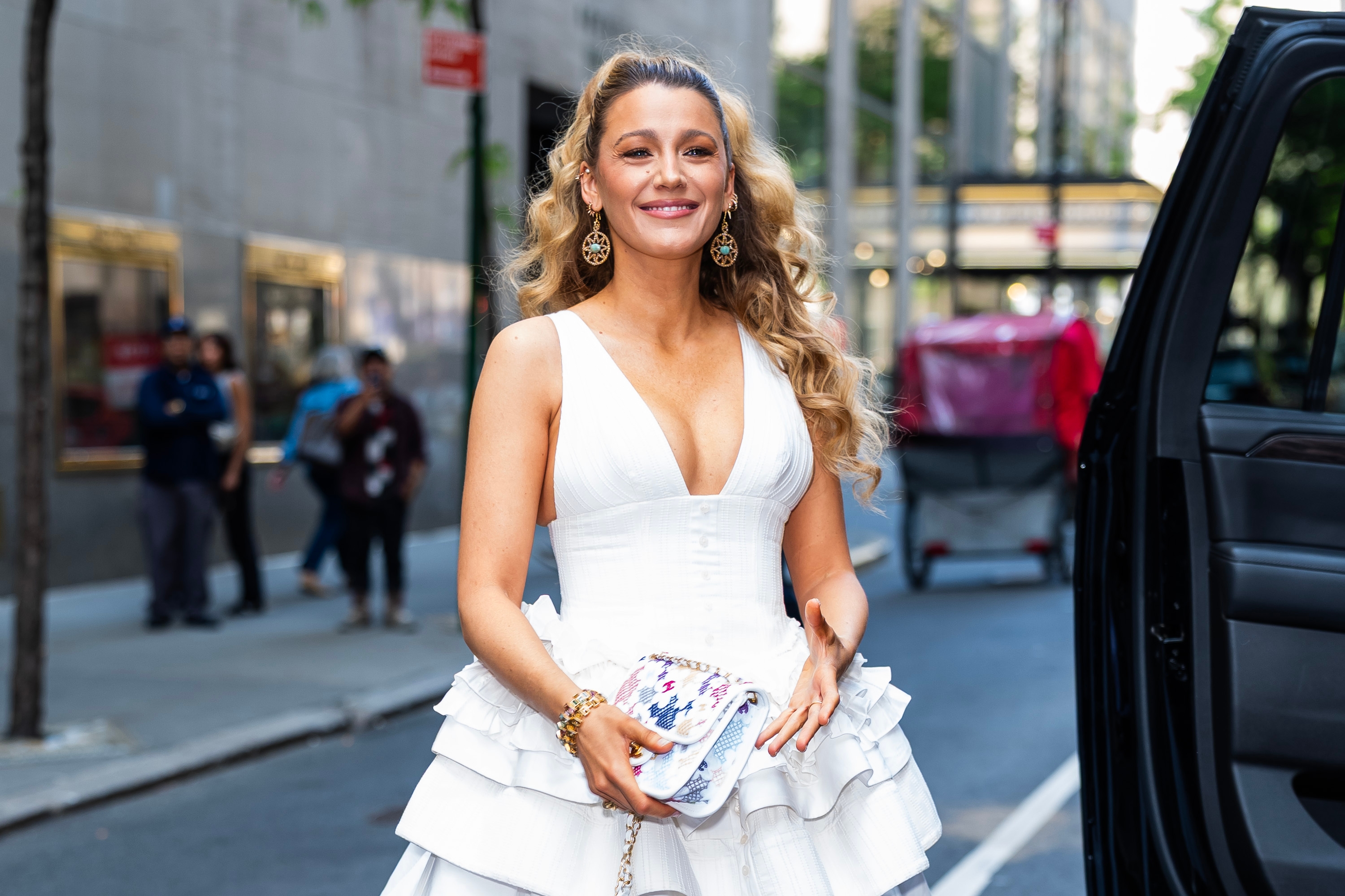 Person in a stylish white tiered dress with a deep neckline, holding a patterned clutch on a city street