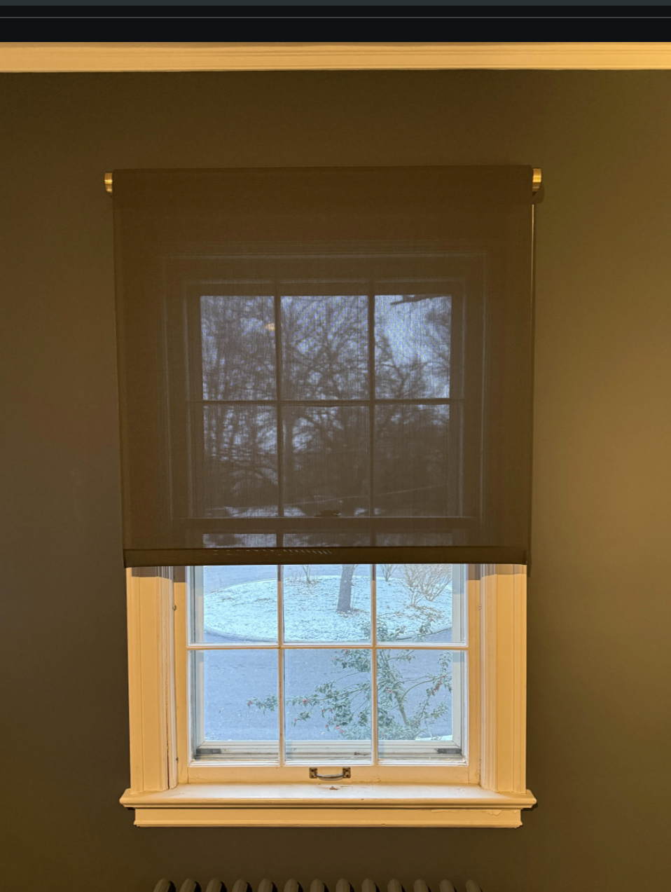 Window with sheer curtain partially drawn, showcasing an exterior view with snow-covered ground outside, underneath a clear blue sky