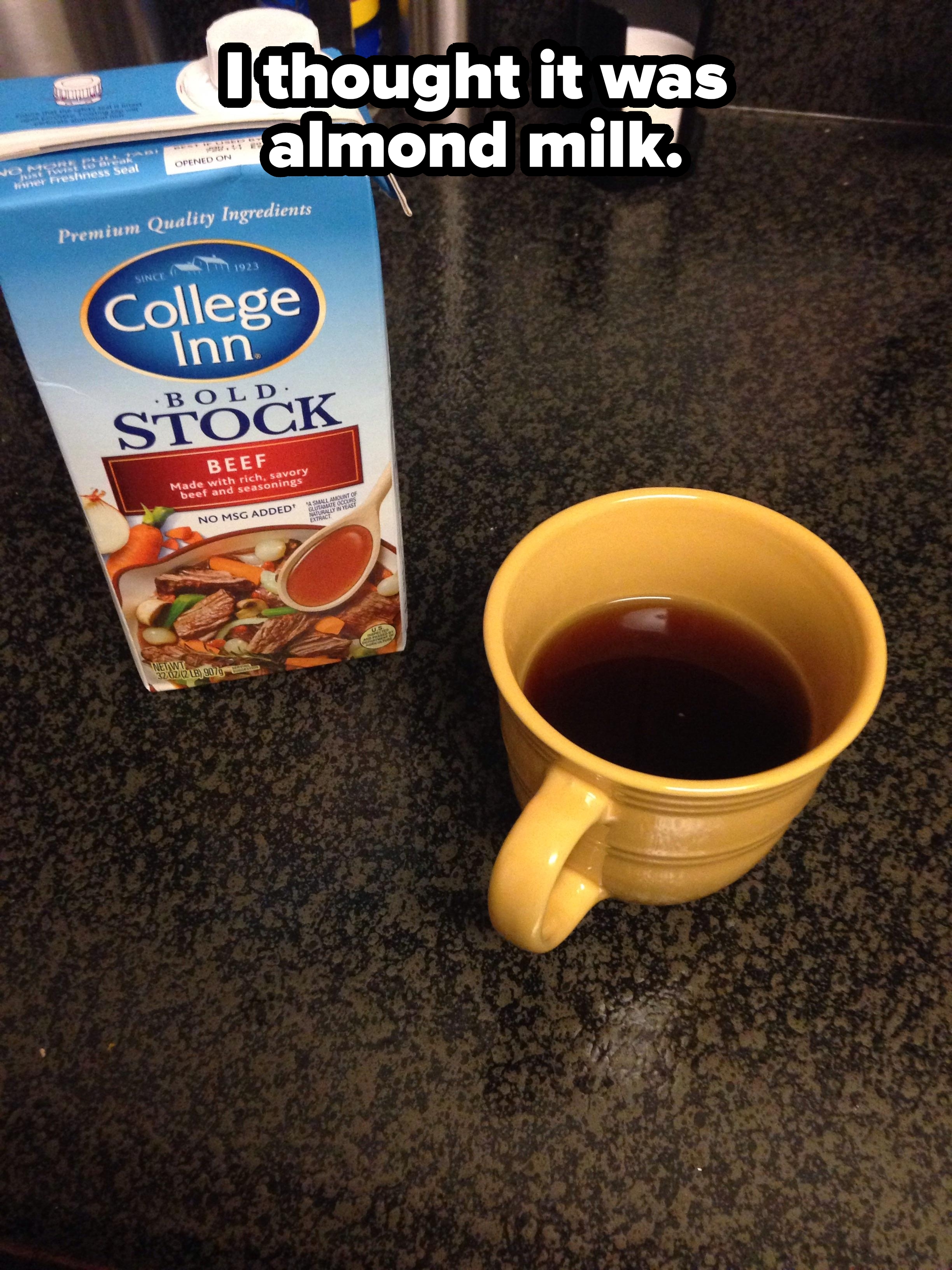 Carton of beef stock next to a filled yellow mug on a countertop