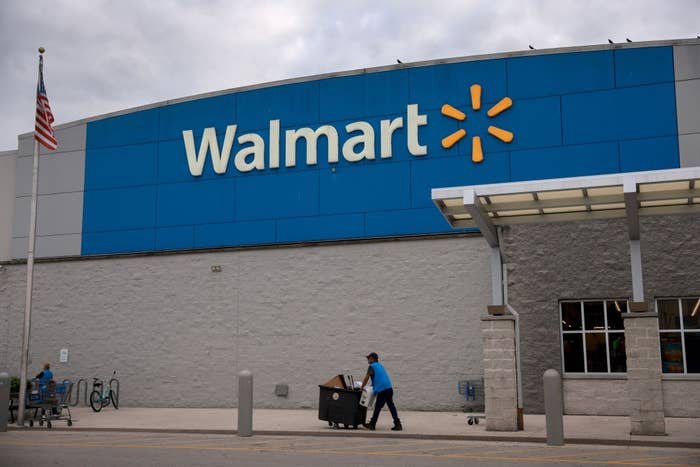 Person in blue uniform pushes a cart outside a Walmart store with a U.S. flag in view