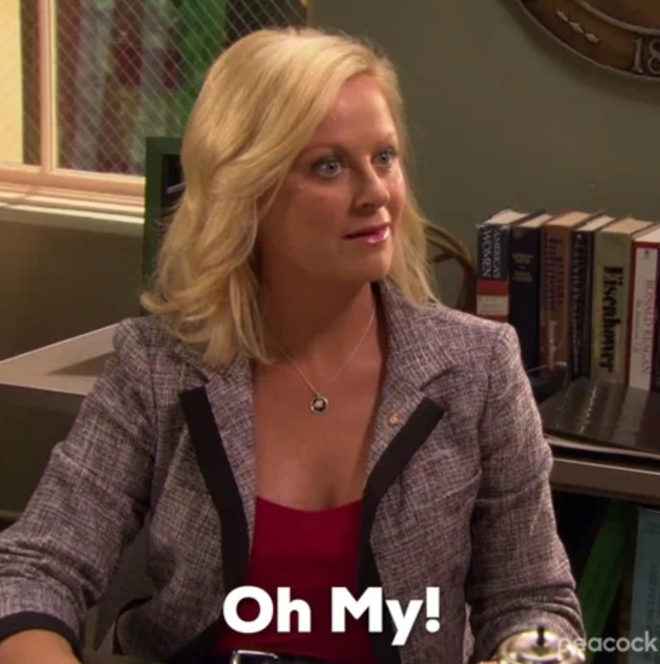 Person sitting at a desk with a surprised expression, wearing a blazer over a top. Text overlay at the bottom reads: "Oh My!"