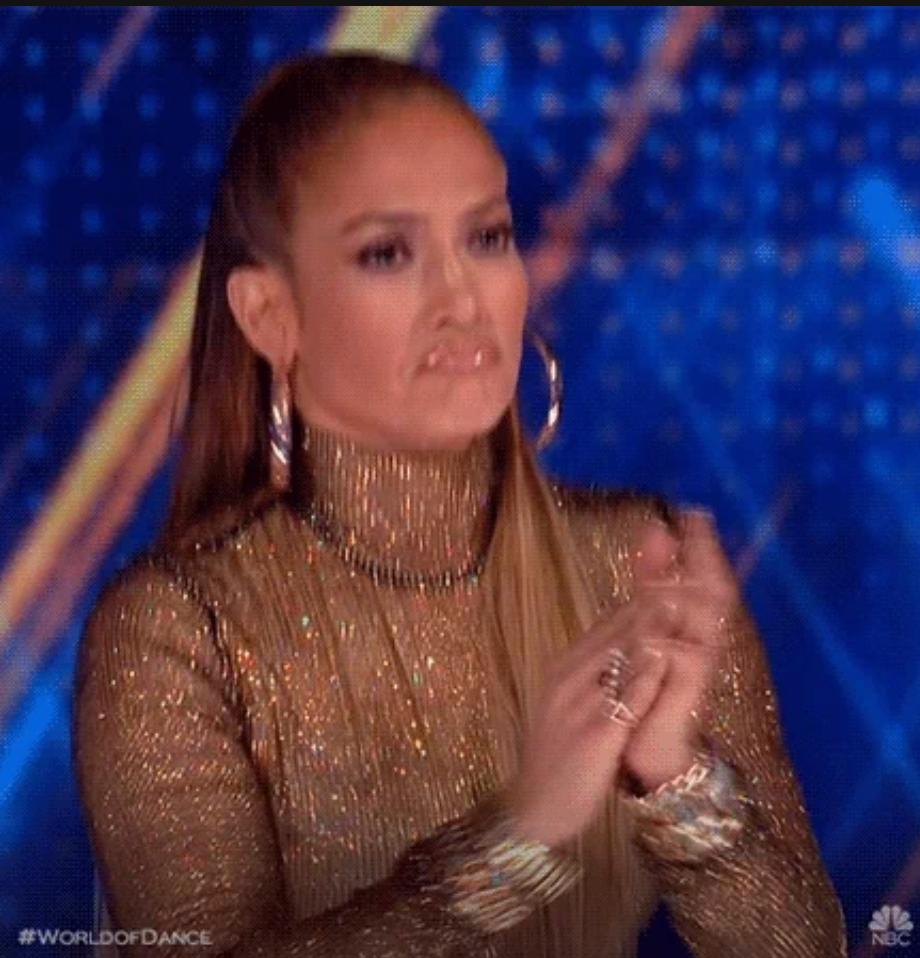 Person clapping, wearing a glittering turtleneck and hoop earrings. Appears to be on a TV show set