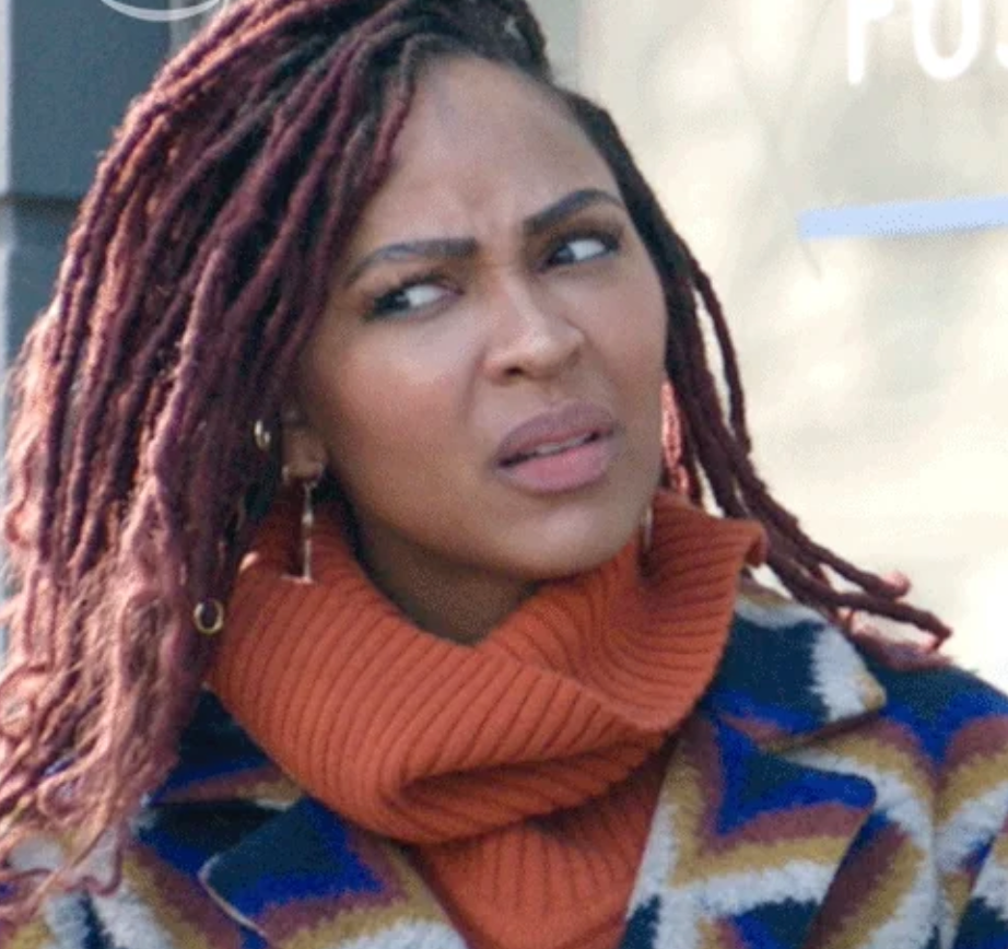 Person with braided hair giving a puzzled expression, wearing a patterned coat and turtleneck