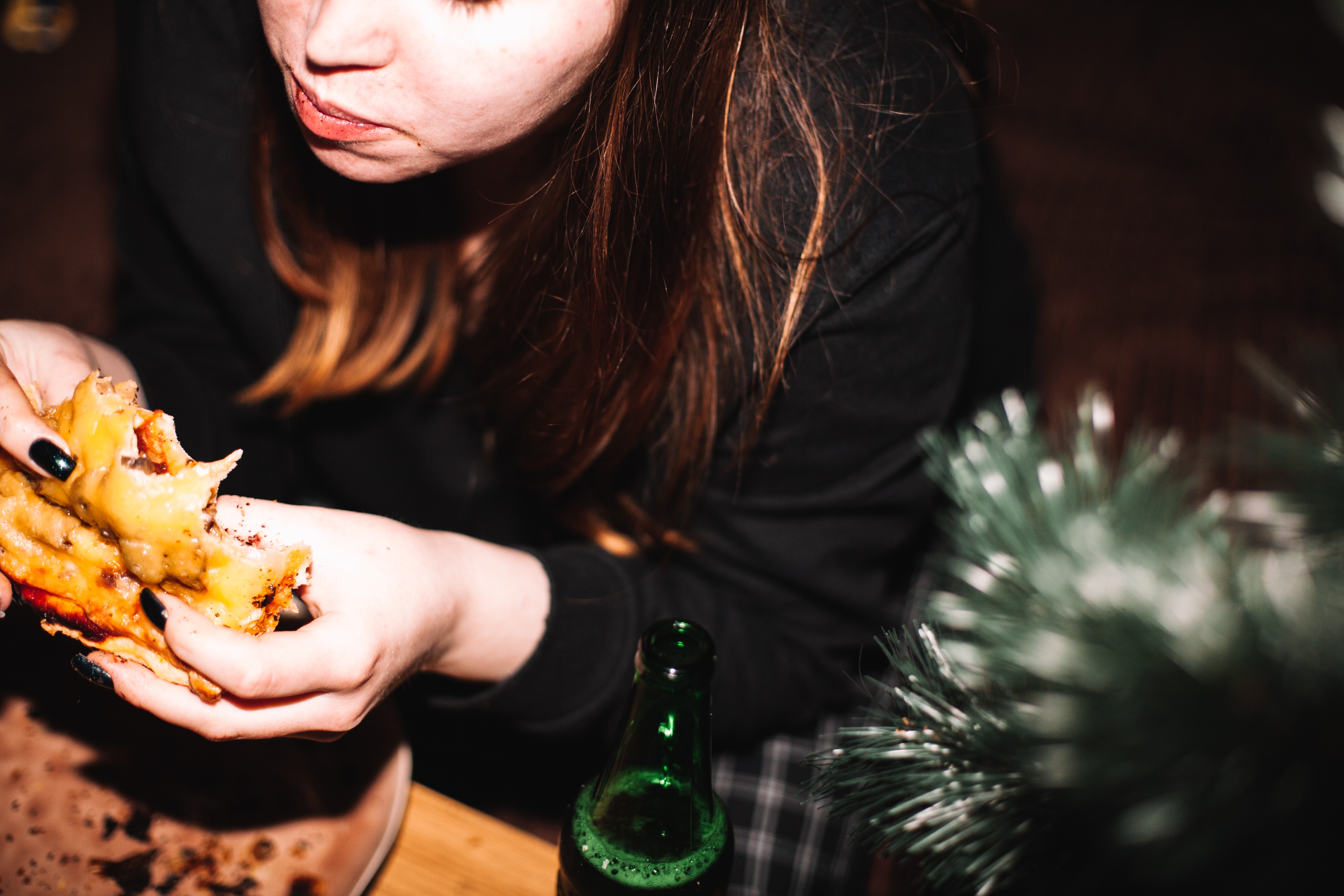 Person eating pizza at a table with a drink bottle nearby and a blurred plant in the foreground