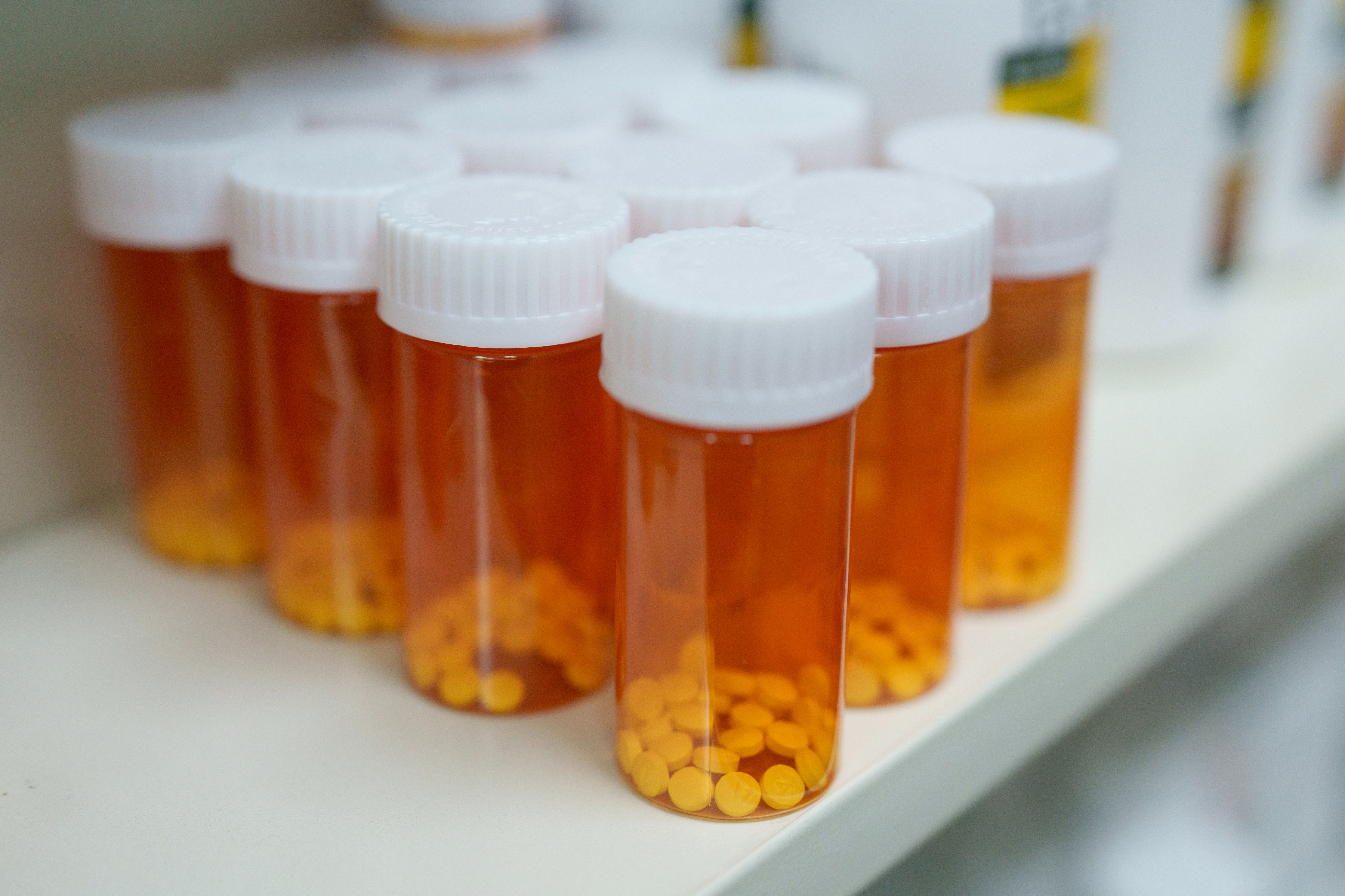 Prescription bottles with white caps, filled with yellow pills, lined up on a shelf