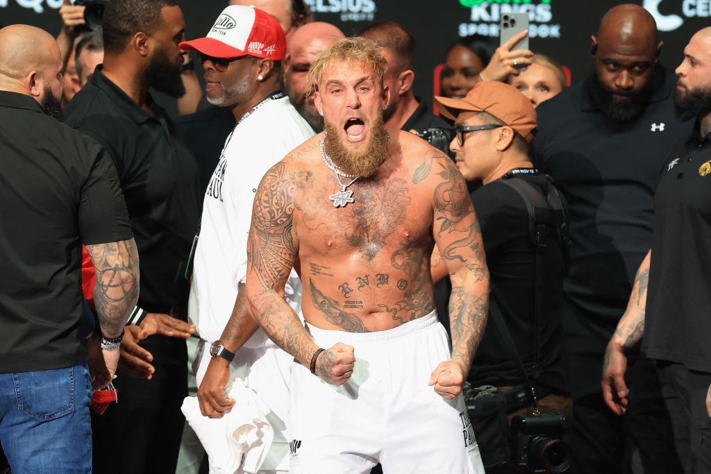 Man with tattoos and shorts on stage, roaring energetically. Surrounding crowd focuses on him, capturing the intense moment