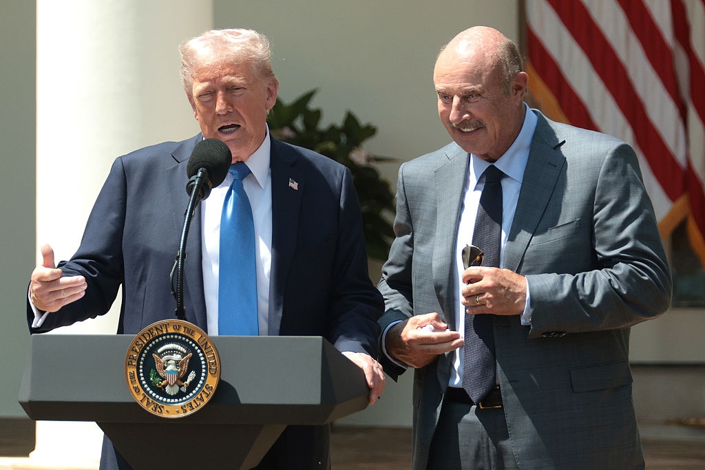 Two men in suits speak at a podium with a presidential seal. An American flag is visible in the background