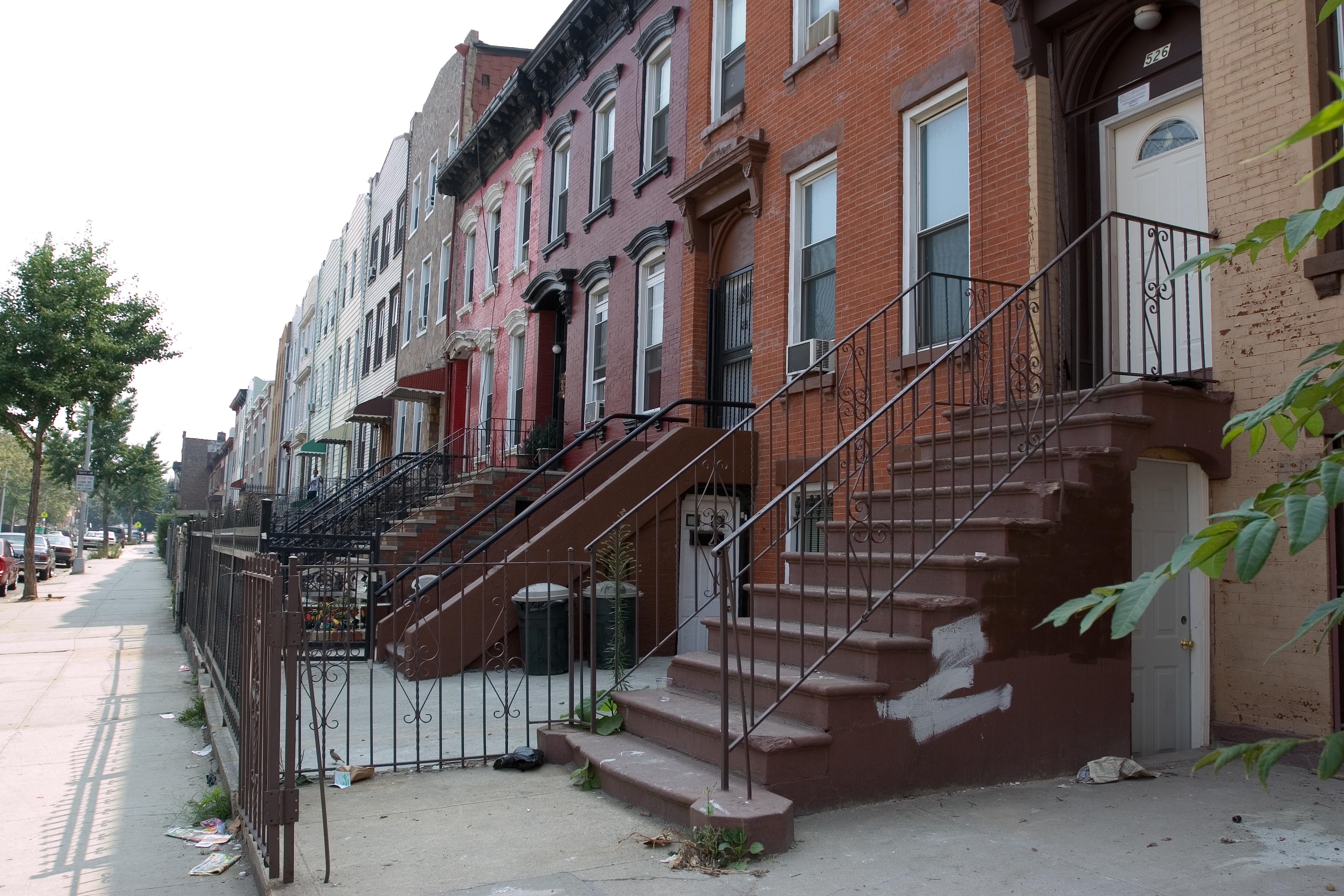 A row of classic urban townhouses with stoops and black iron railings lining a quiet street