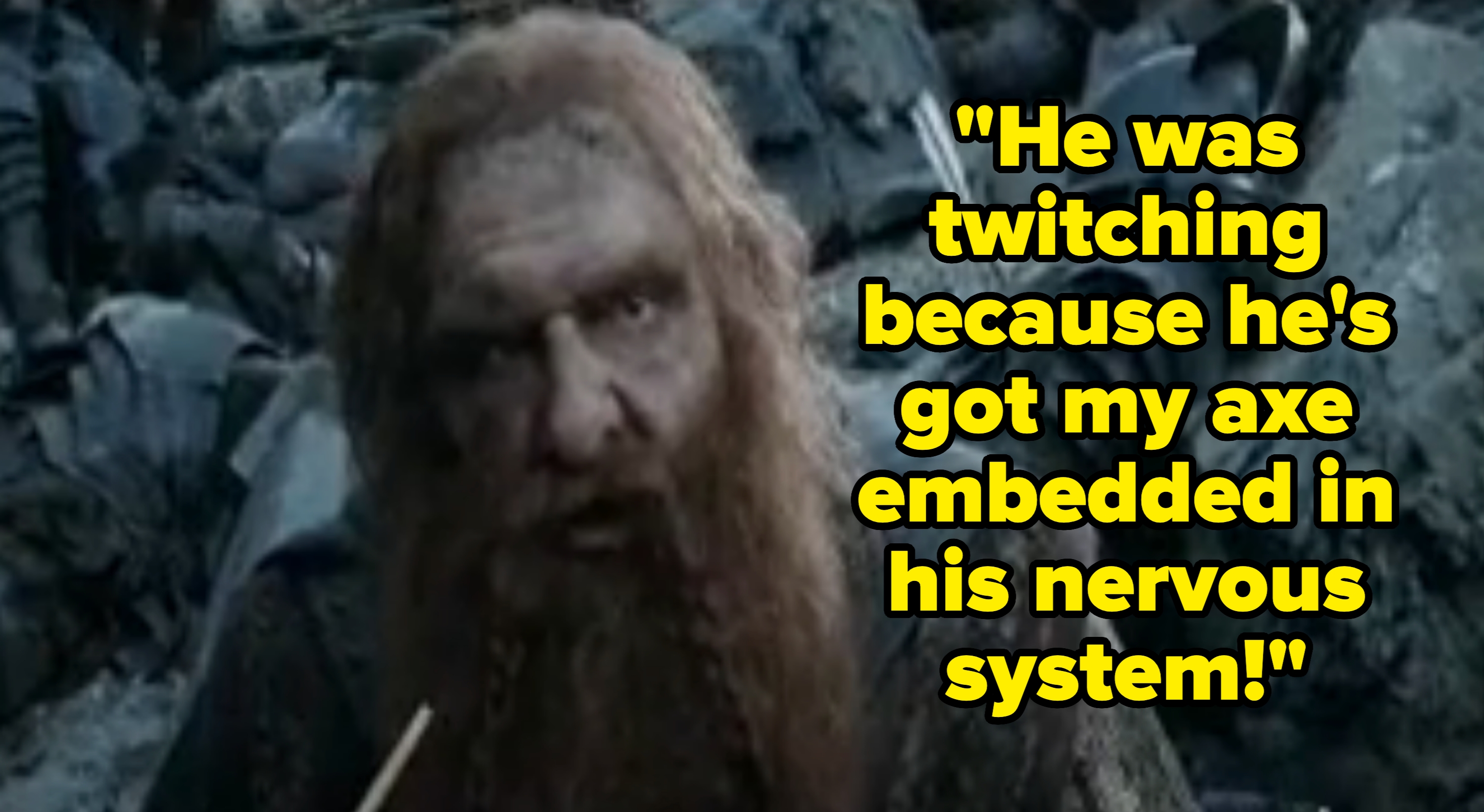 A character with long hair and a beard is in a battle scene with armor in the background, holding a weapon