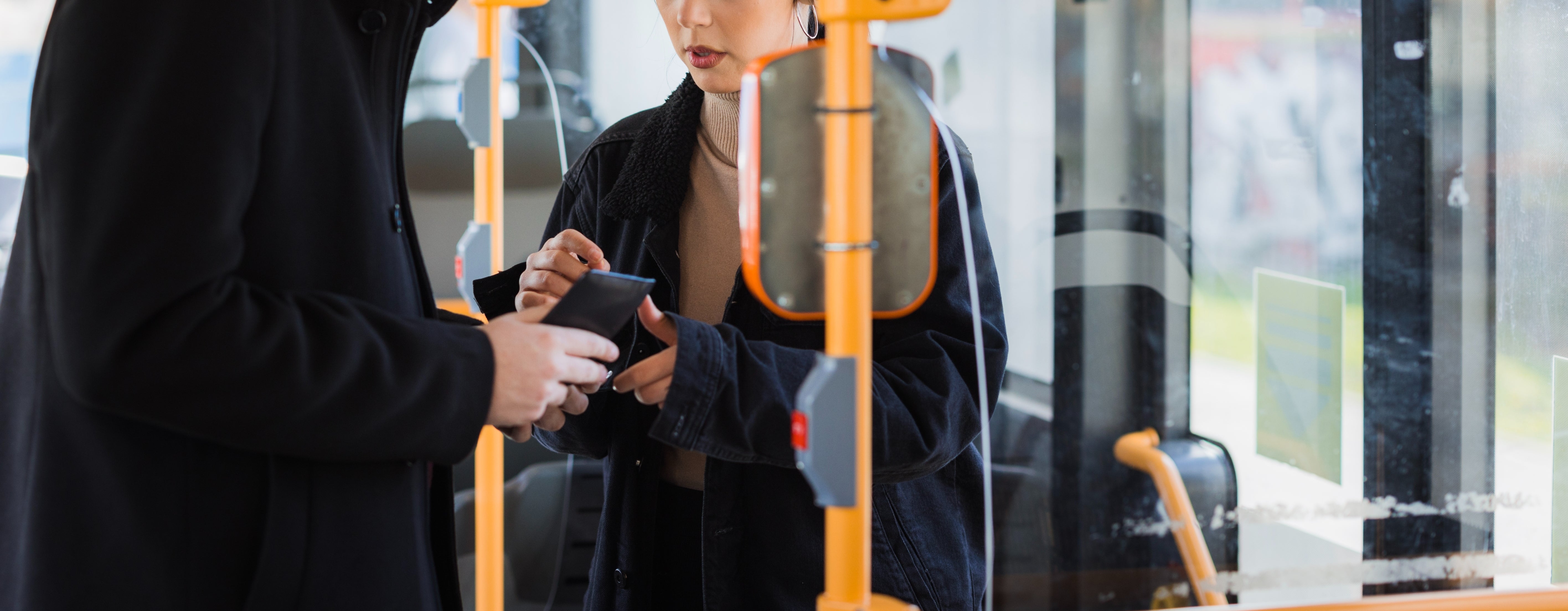 Two people in a bus, standing near the driver's area, discussing or looking at a ticket or document