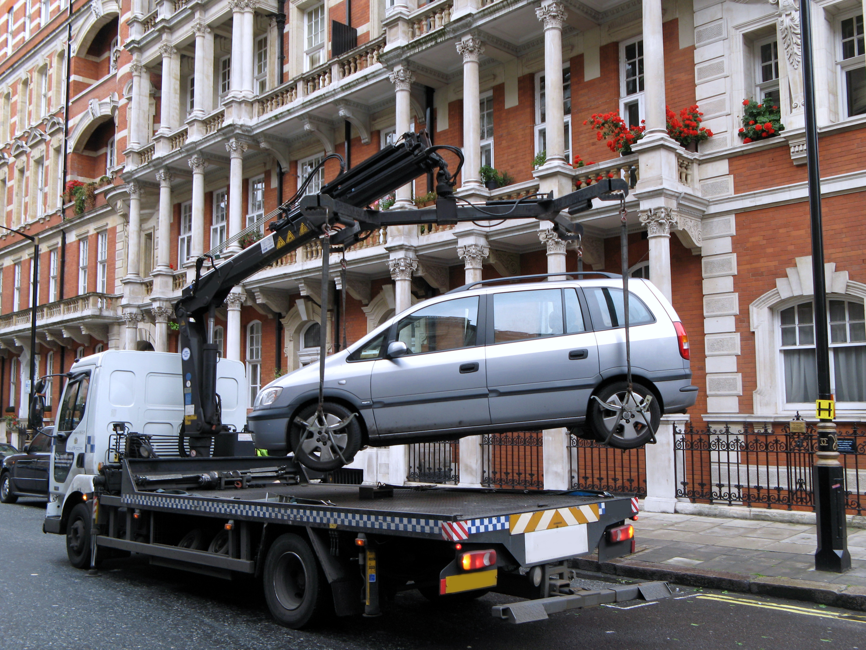 Tow truck lifting a van on a city street in front of ornate buildings with balconies and flowers