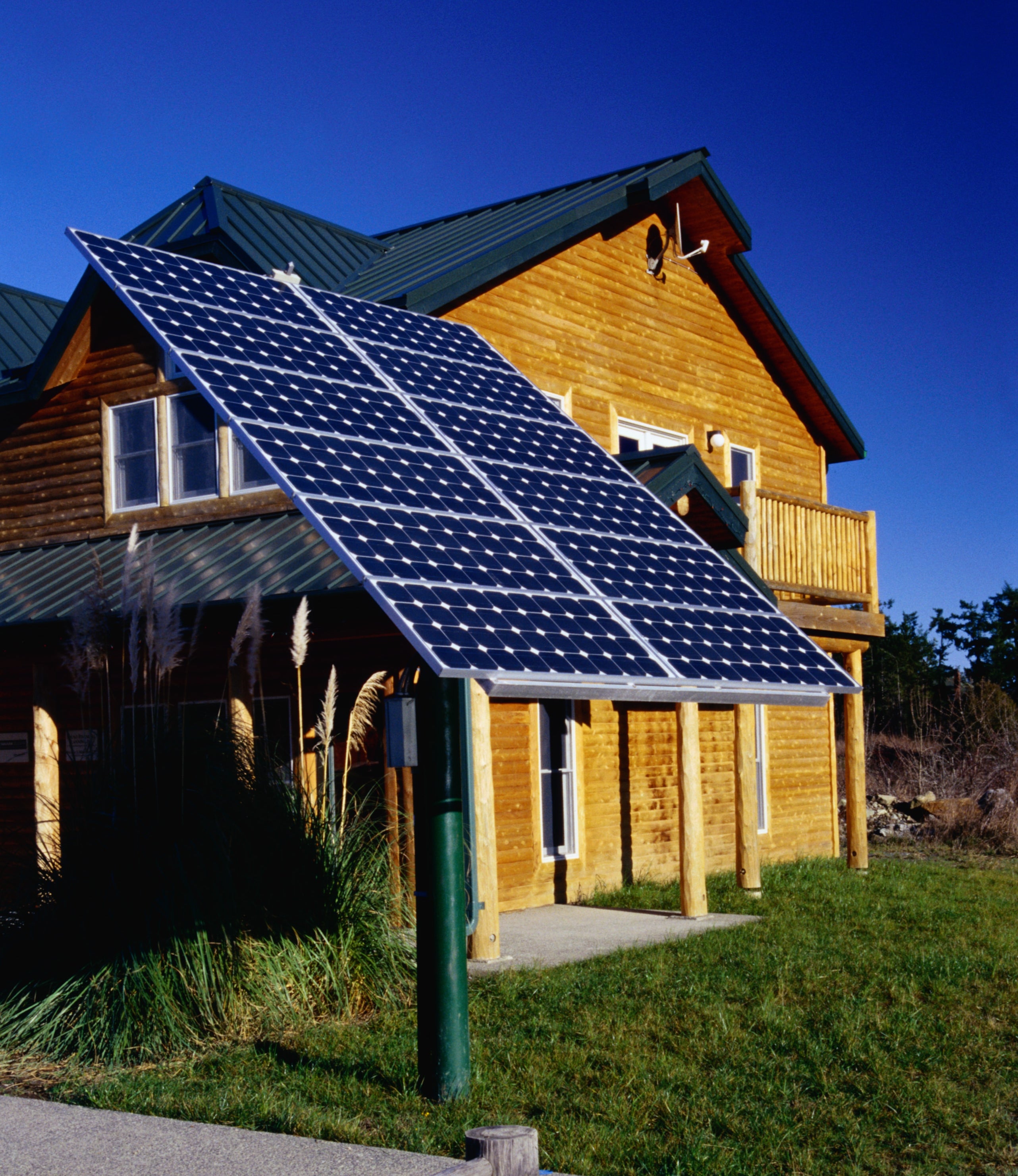 A wooden house with a large solar panel installation in the front yard under a clear sky