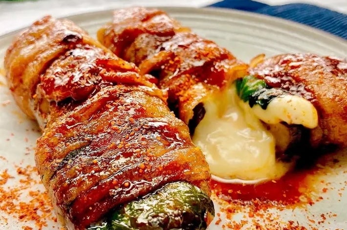 豚肉で巻かれたなすの中からチーズが溶け出している料理が皿に盛られている。