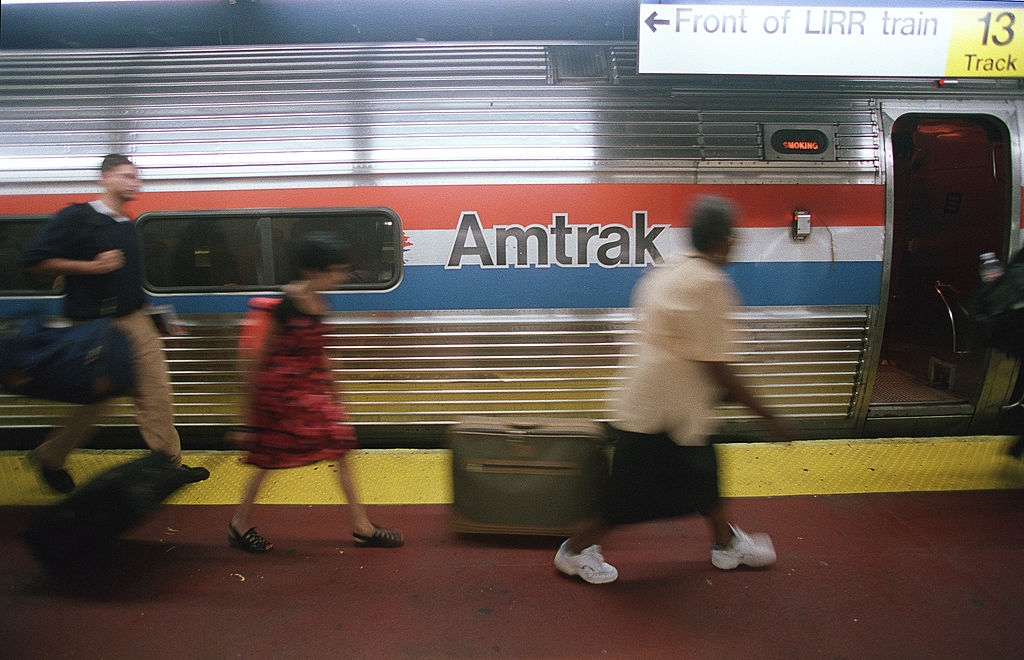 People rushing on a train platform beside an Amtrak train. One carries luggage, while the train is ready for boarding