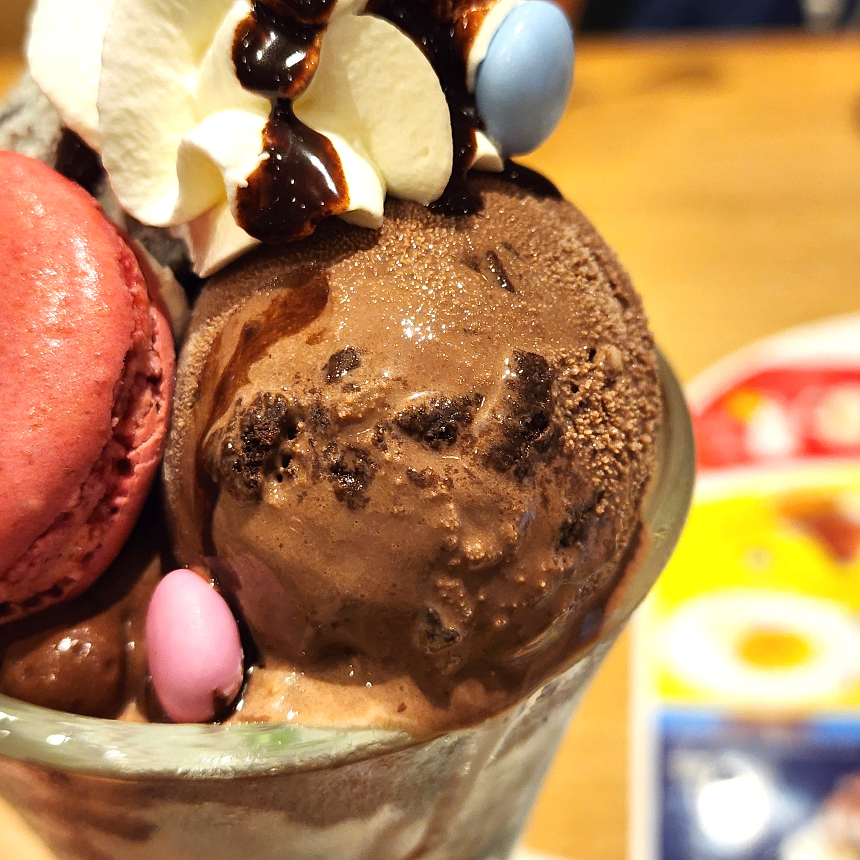 チョコレートアイスクリーム、ホイップクリーム、カラフルなマカロンとチョコレートソースでトッピングされたデザート。