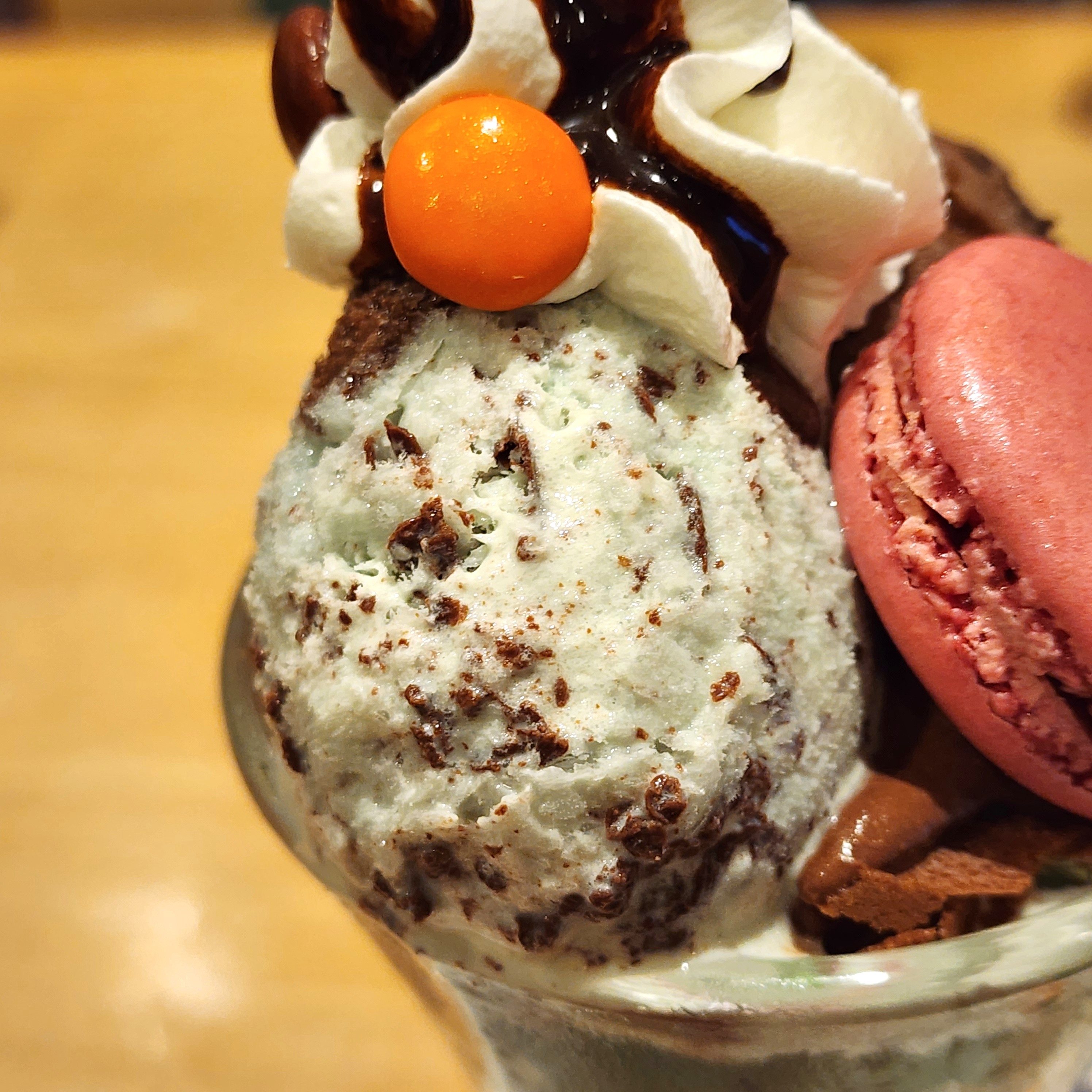 パフェのアップ写真。アイスクリーム、ホイップクリーム、オレンジ色の飾り、赤いマカロンが載っている。