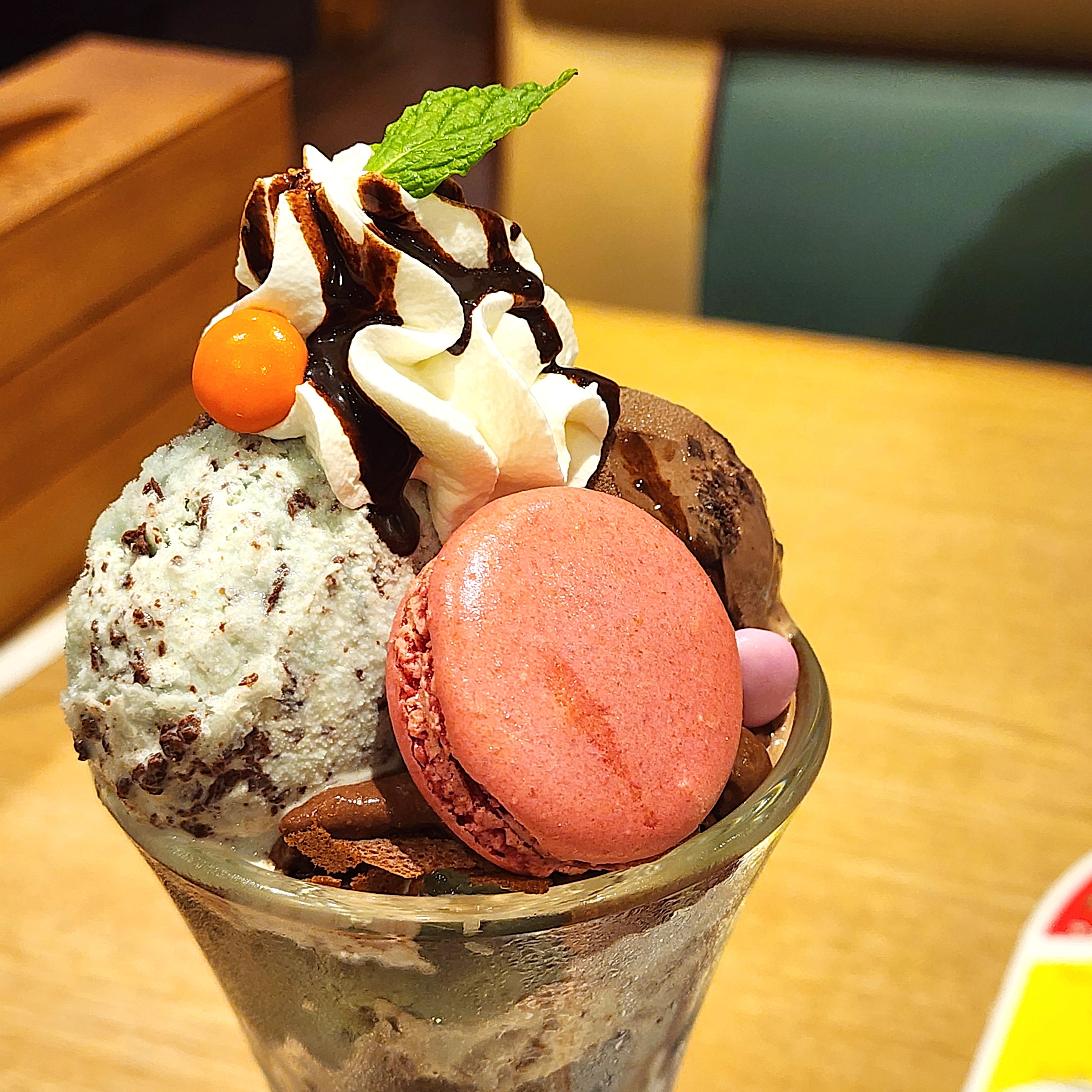 アイスクリームパフェ、チョコソース、ピンクのマカロン、ミントの葉がトッピングされているデザート。