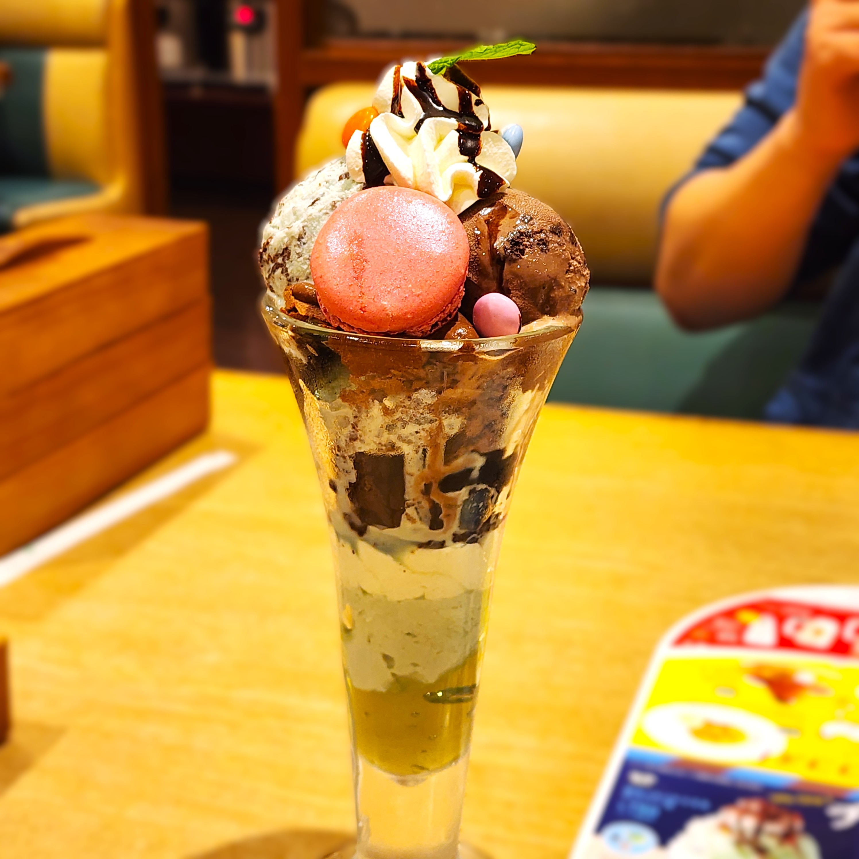 パフェにチョコレートソース、ホイップクリーム、マカロン、アイスクリームがトッピングされています。