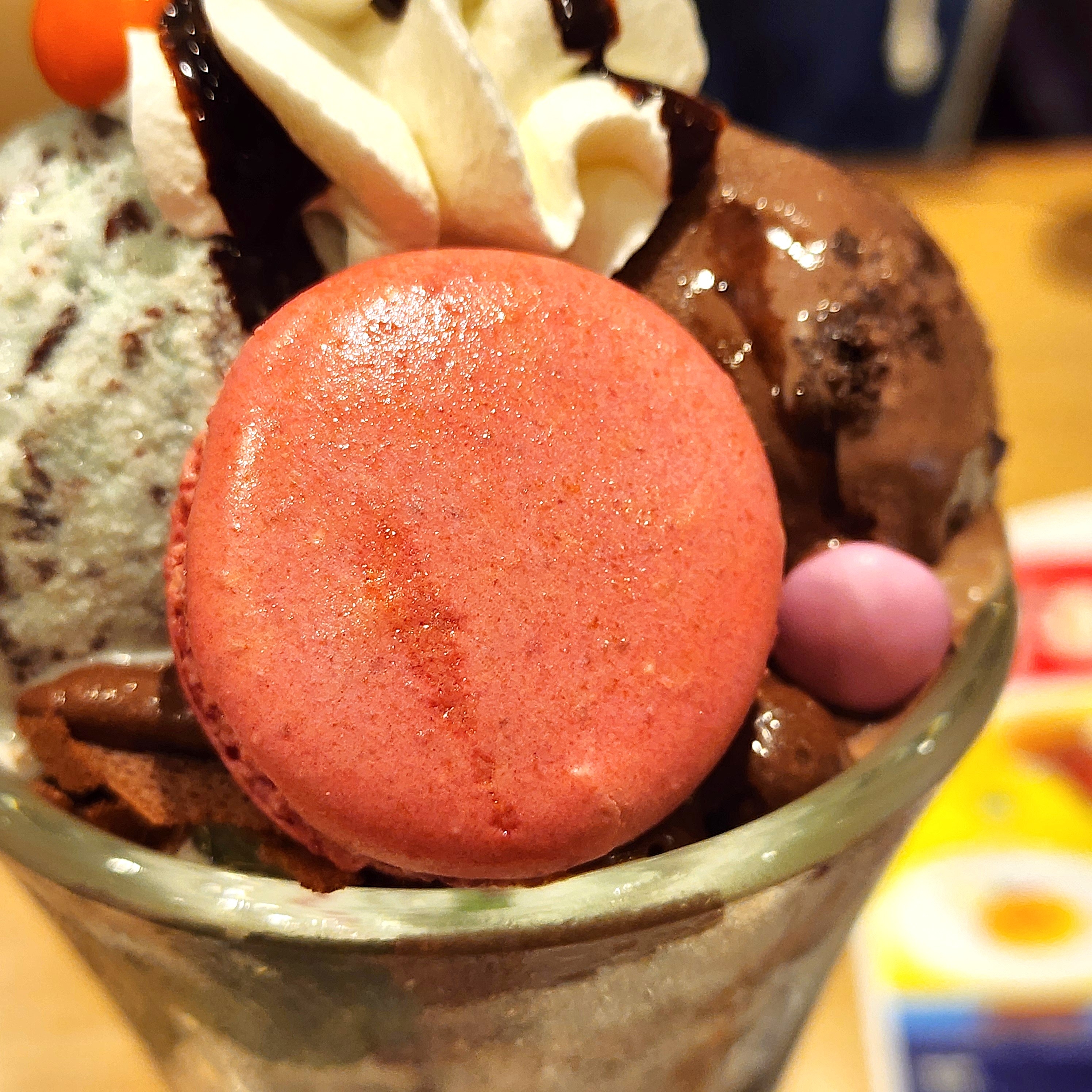 パフェの上にマカロン、クリーム、チョコレートソースが載っています。デザートの広告用イメージです。