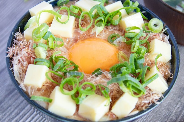 卵、チーズ、ネギがトッピングされたご飯のボウル。食事がセットされたテーブル上。