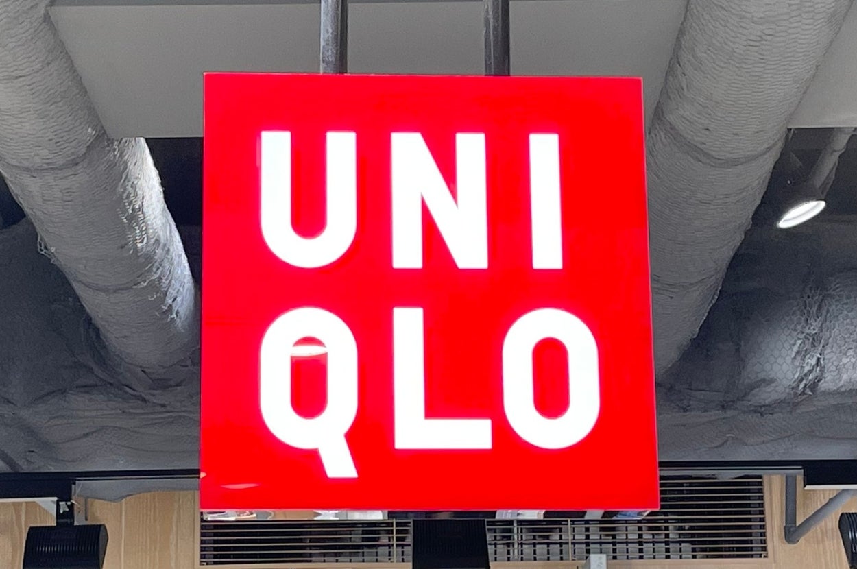 Red Uniqlo sign hanging from the ceiling in a retail store, with folded clothing displayed on shelves below