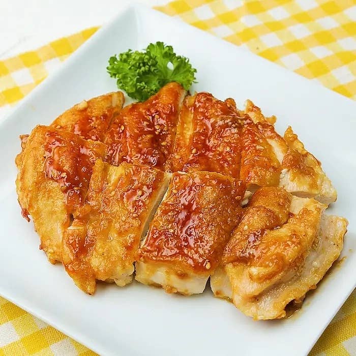 料理の画像には、白い皿に盛られた照り焼きチキンとパセリの添え物があります。