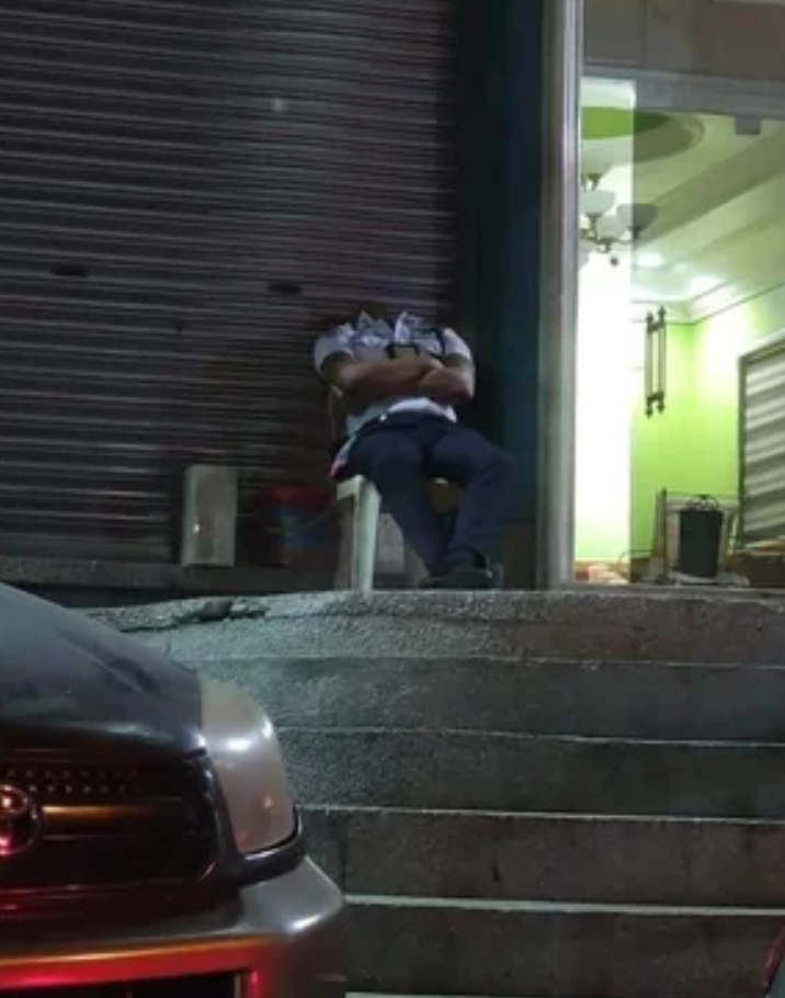 A person is sleeping while sitting on steps outside a closed storefront at night