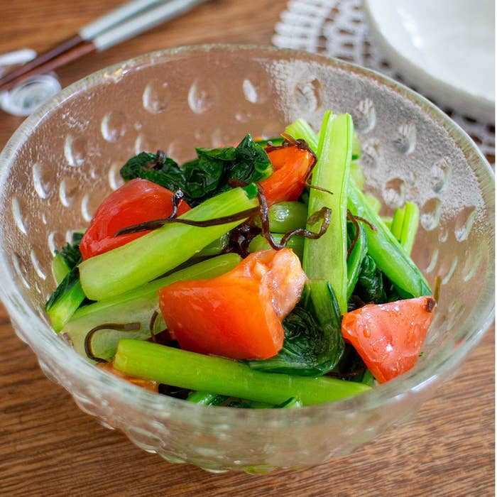 ガラスボウルに盛られたトマトと緑の野菜のサラダ。食卓が背景に見える。