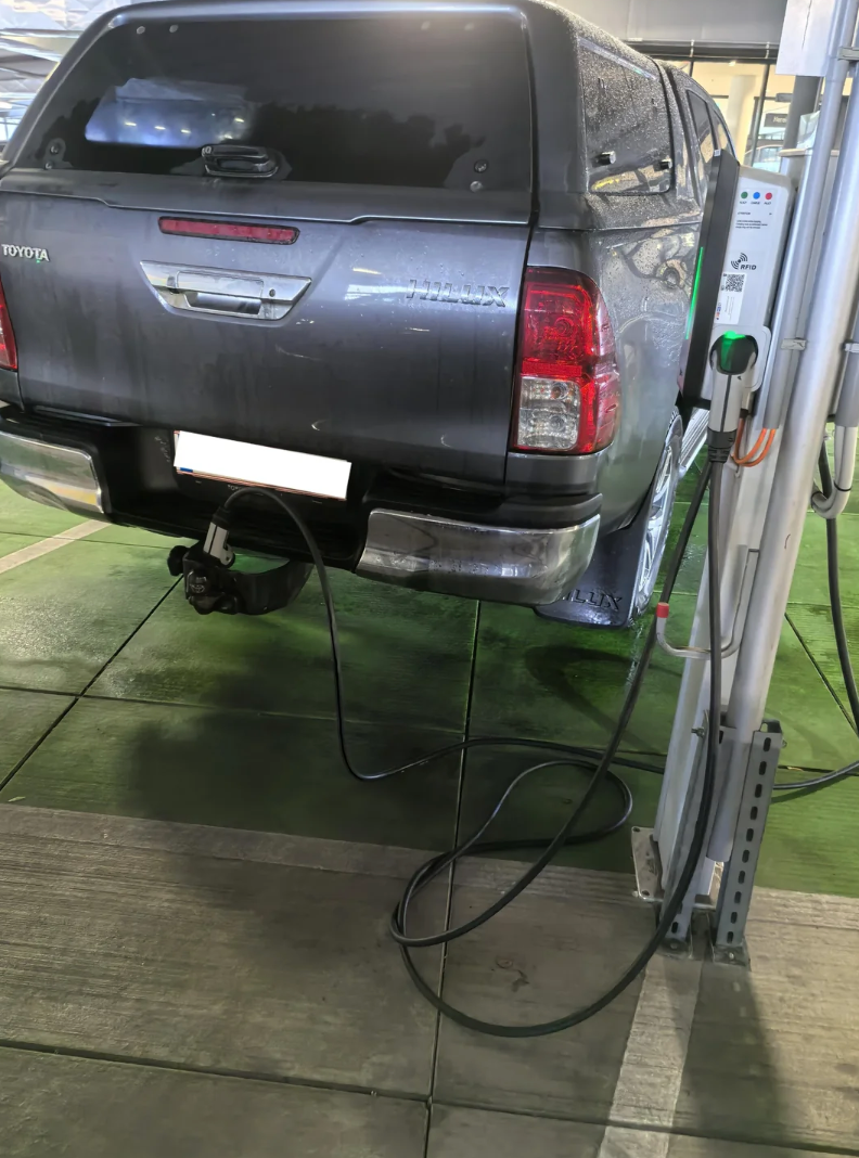 A pickup truck is parked in an electric vehicle charging station, connected to a charger