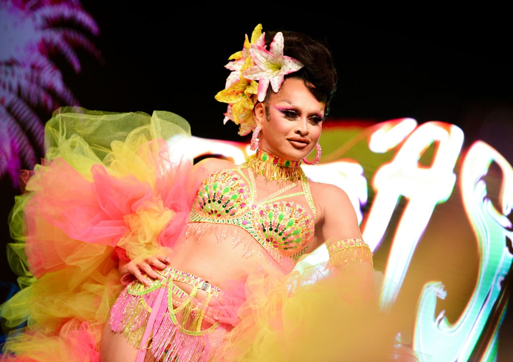 Person in vibrant, tropical-inspired costume with beaded accents and floral headpiece poses at a public event