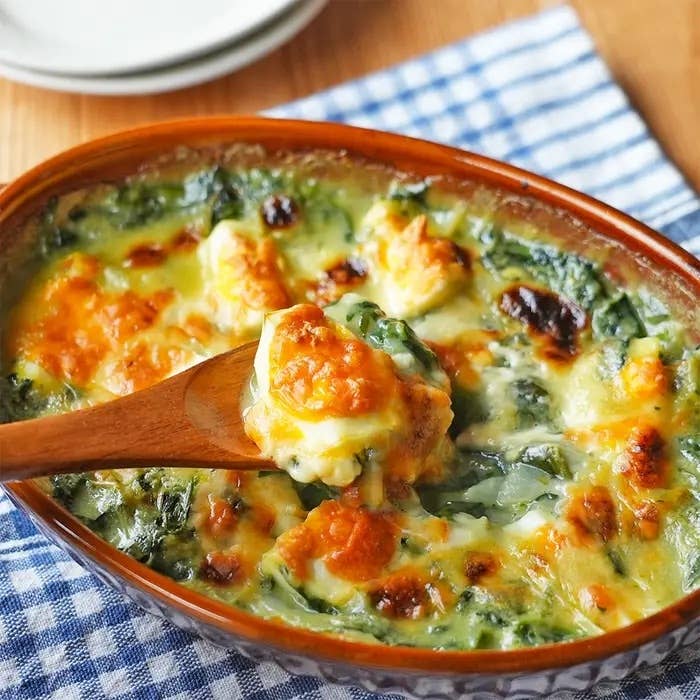 ホウレンソウとチーズのグラタンがテーブルにのっており、木のスプーンで一部がすくわれています。