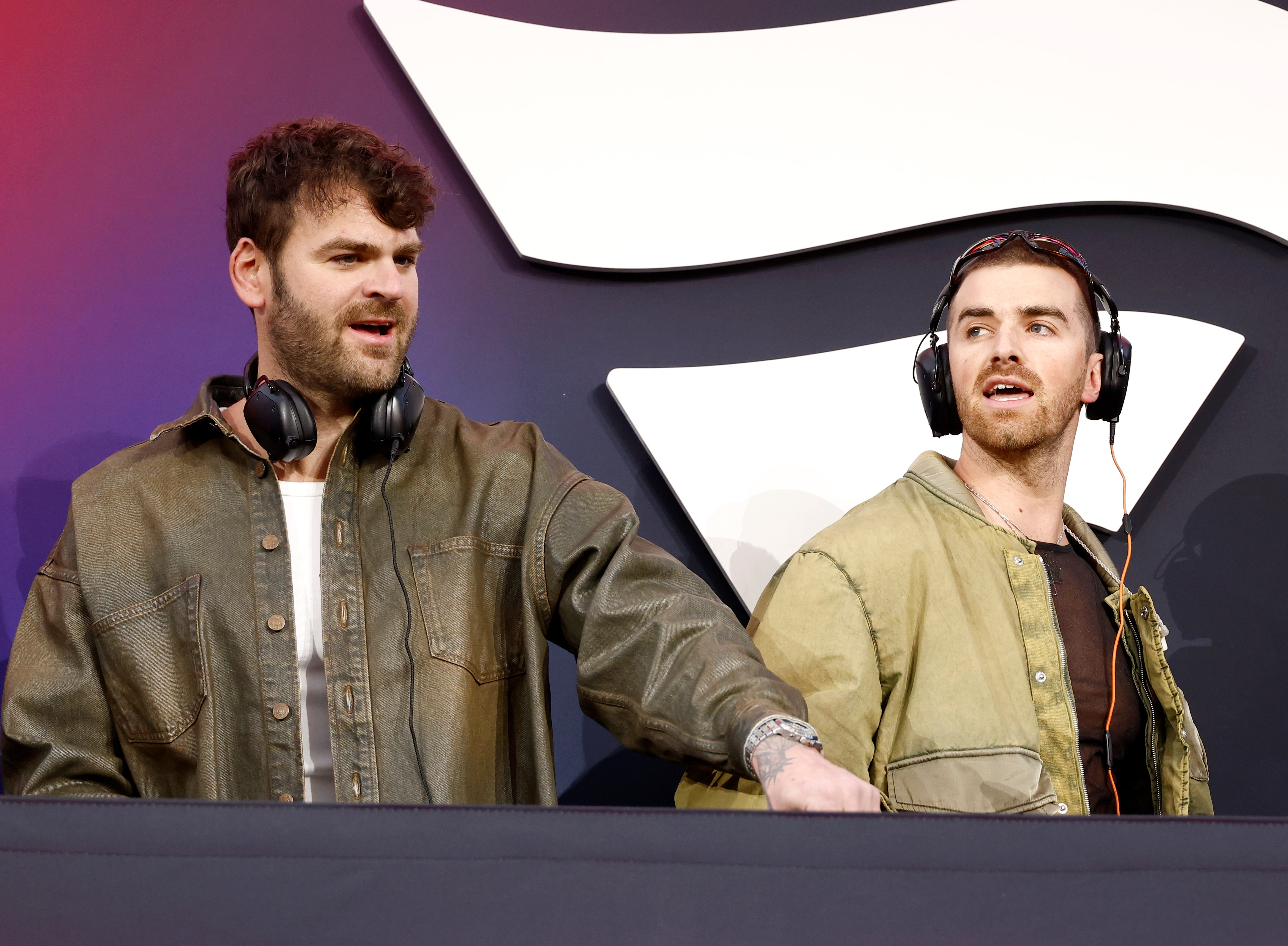 The Chainsmokers wearing headphones stanidng behind a DJ booth
