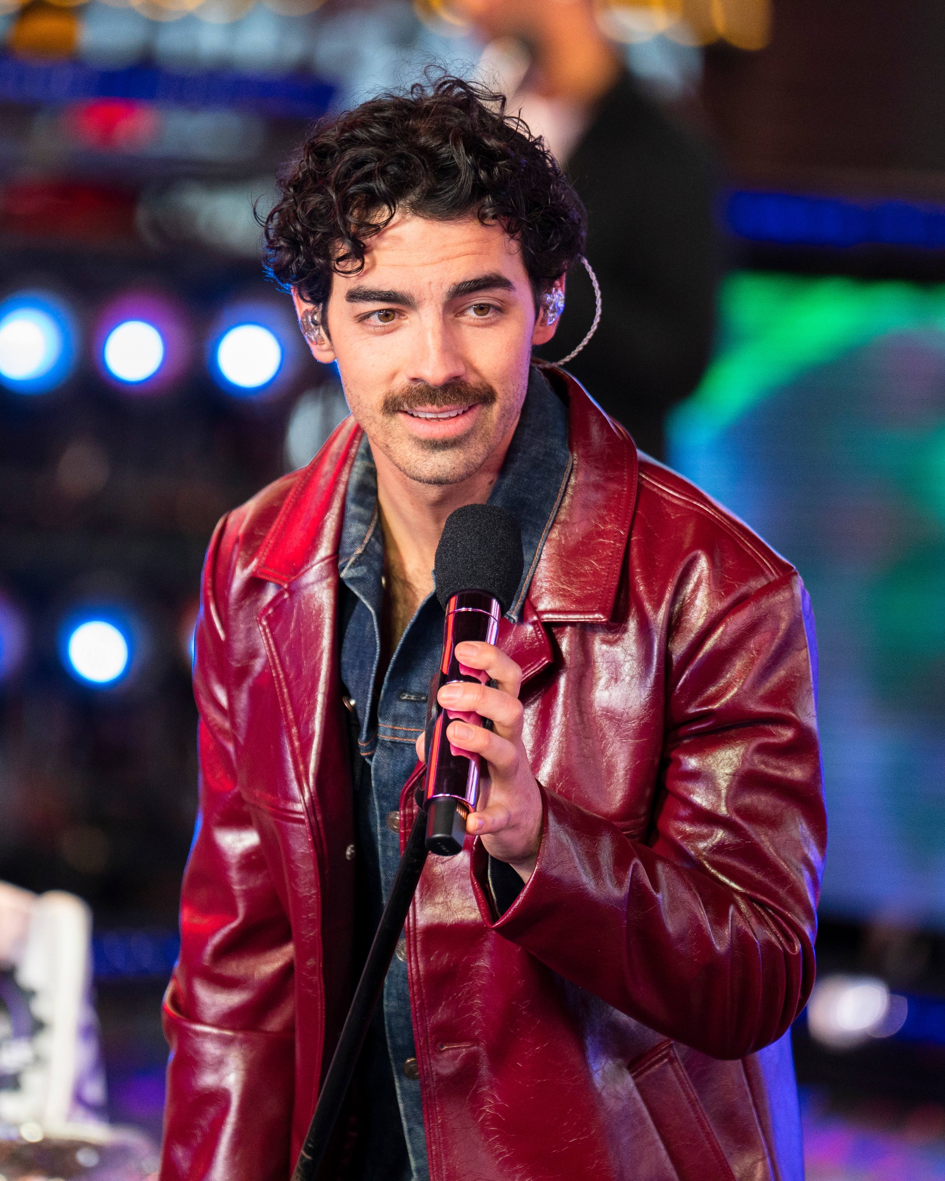 Joe Jonas holding a microphone on stage at a public event