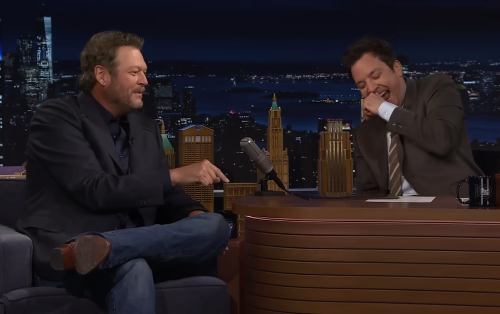 Blake Shelton and Jimmy Fallon laughing during an interview on a late-night talk show set