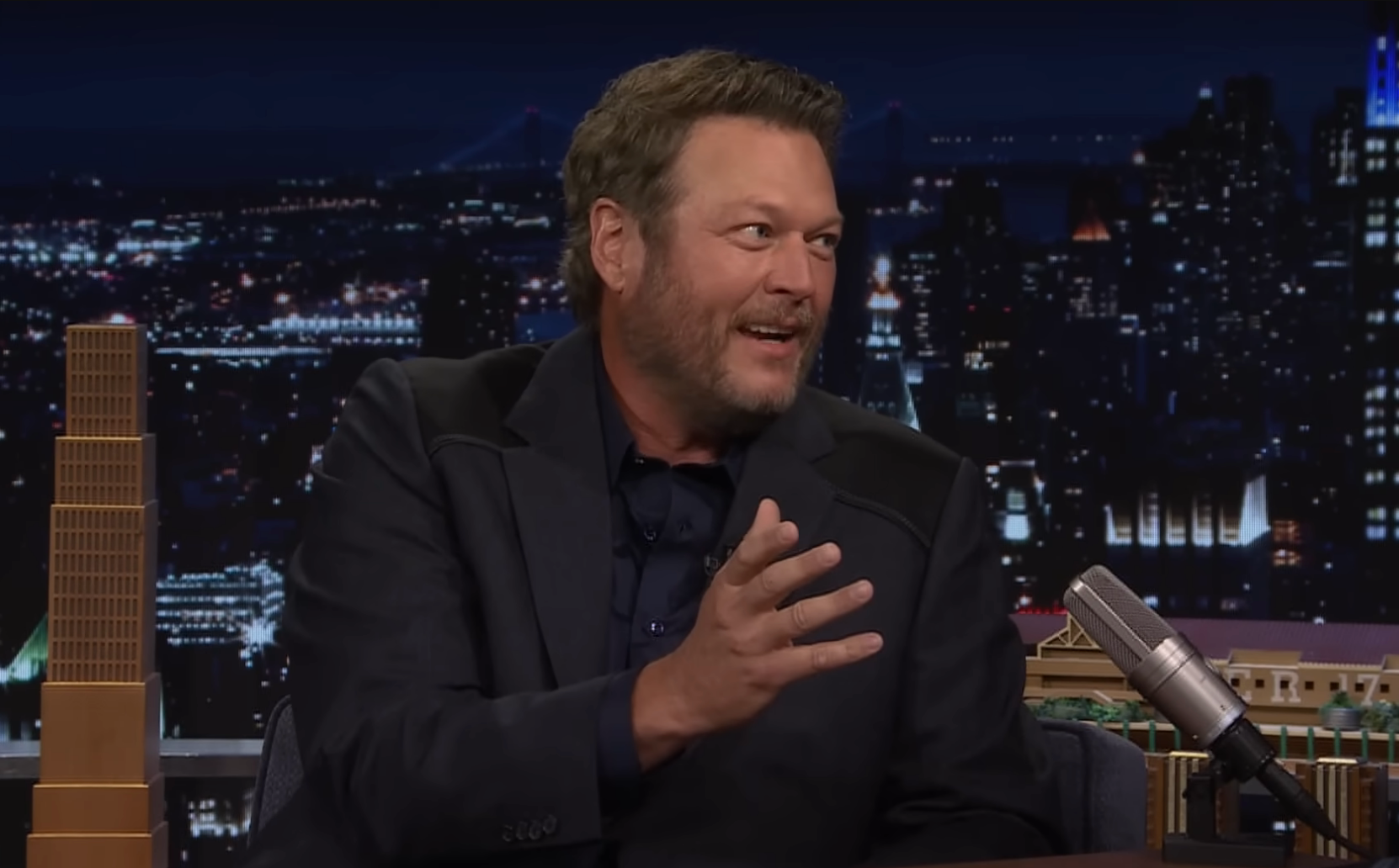 Blake Shelton talking animatedly on a late-night show set