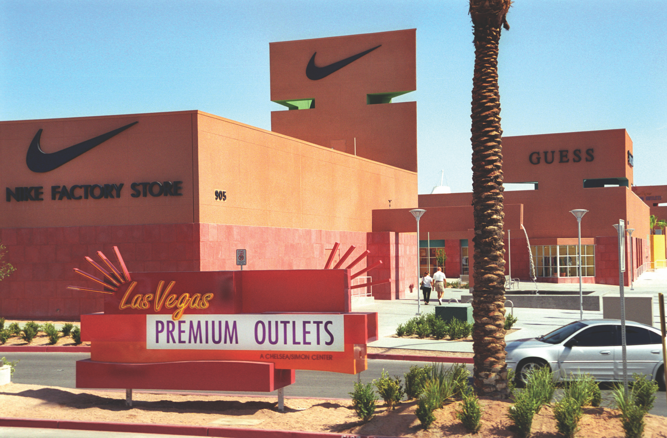 Exterior view of Las Vegas Premium Outlets featuring Nike and Guess stores with palm trees and a visible parking area