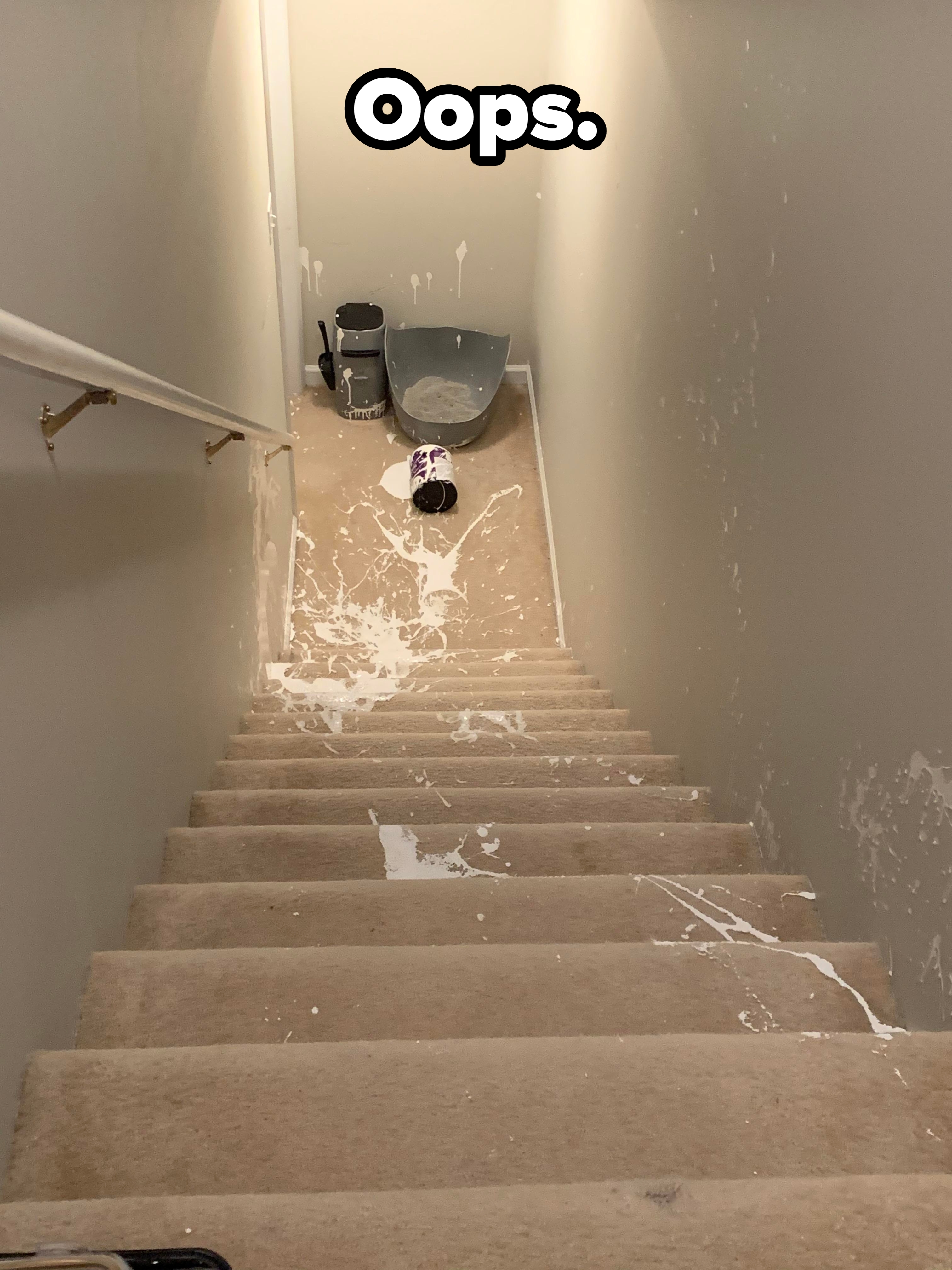 Spilled white paint covers carpeted stairs, with an overturned can and painting supplies at the base