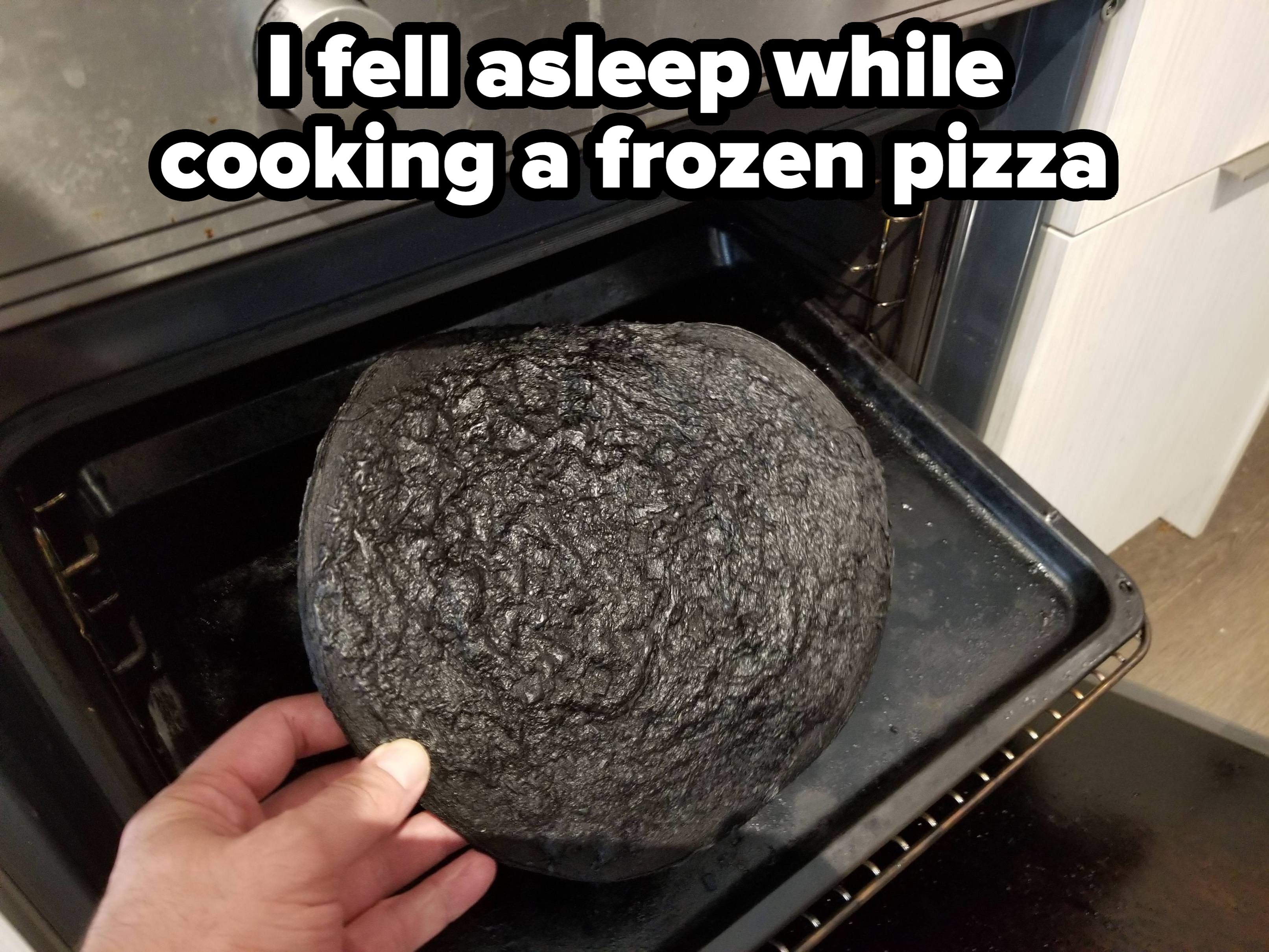 A person holds a visibly burnt pizza on a tray just taken out of the oven, showcasing a cooking mishap