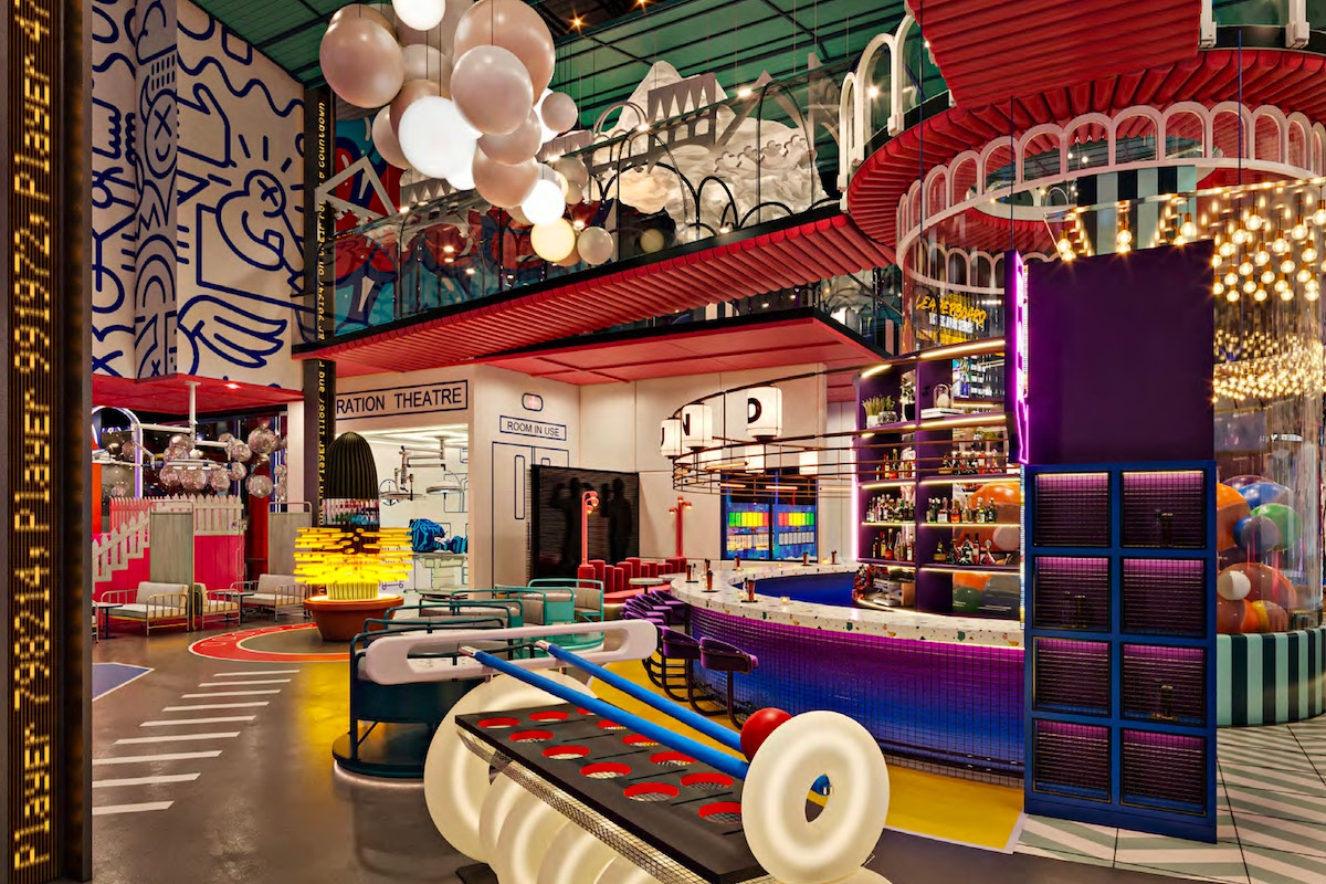 Playful, vibrant indoor space with eclectic decor, featuring a foosball table, colorful seating, and a bar area illuminated by bright lights