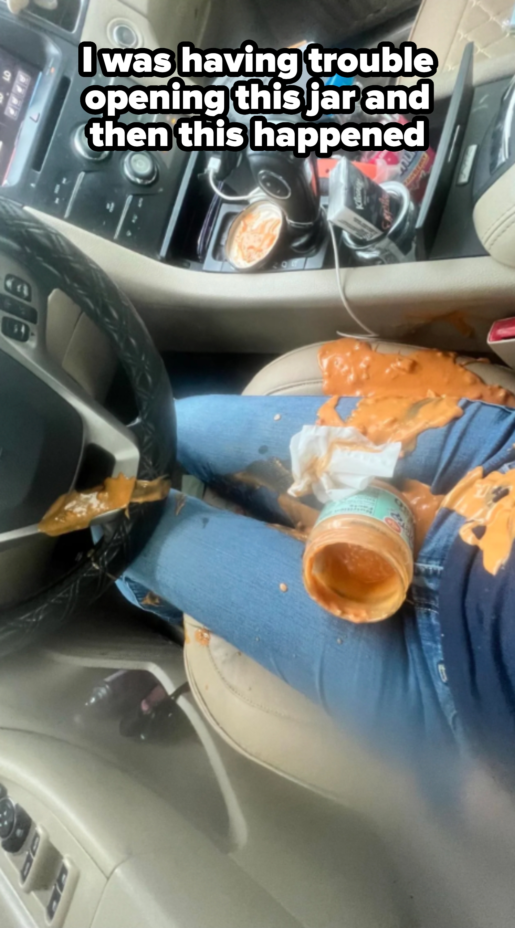 Spilled jar of sauce on car seat and jeans, with sauce splattered on center console and steering wheel