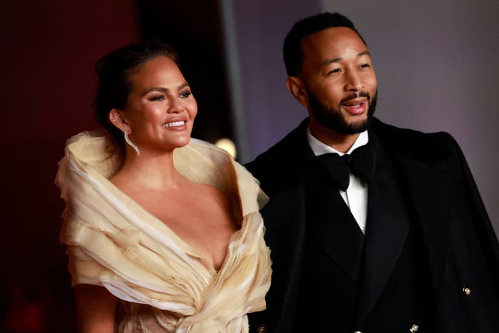 A celebrity couple on the red carpet; the woman wears an elegant off-shoulder gown, and the man is in a classic tuxedo with a bow tie
