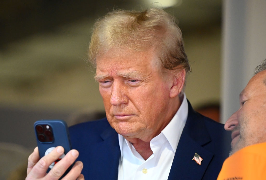 A person in a suit with a flag pin is looking intently at a smartphone screen in a candid moment