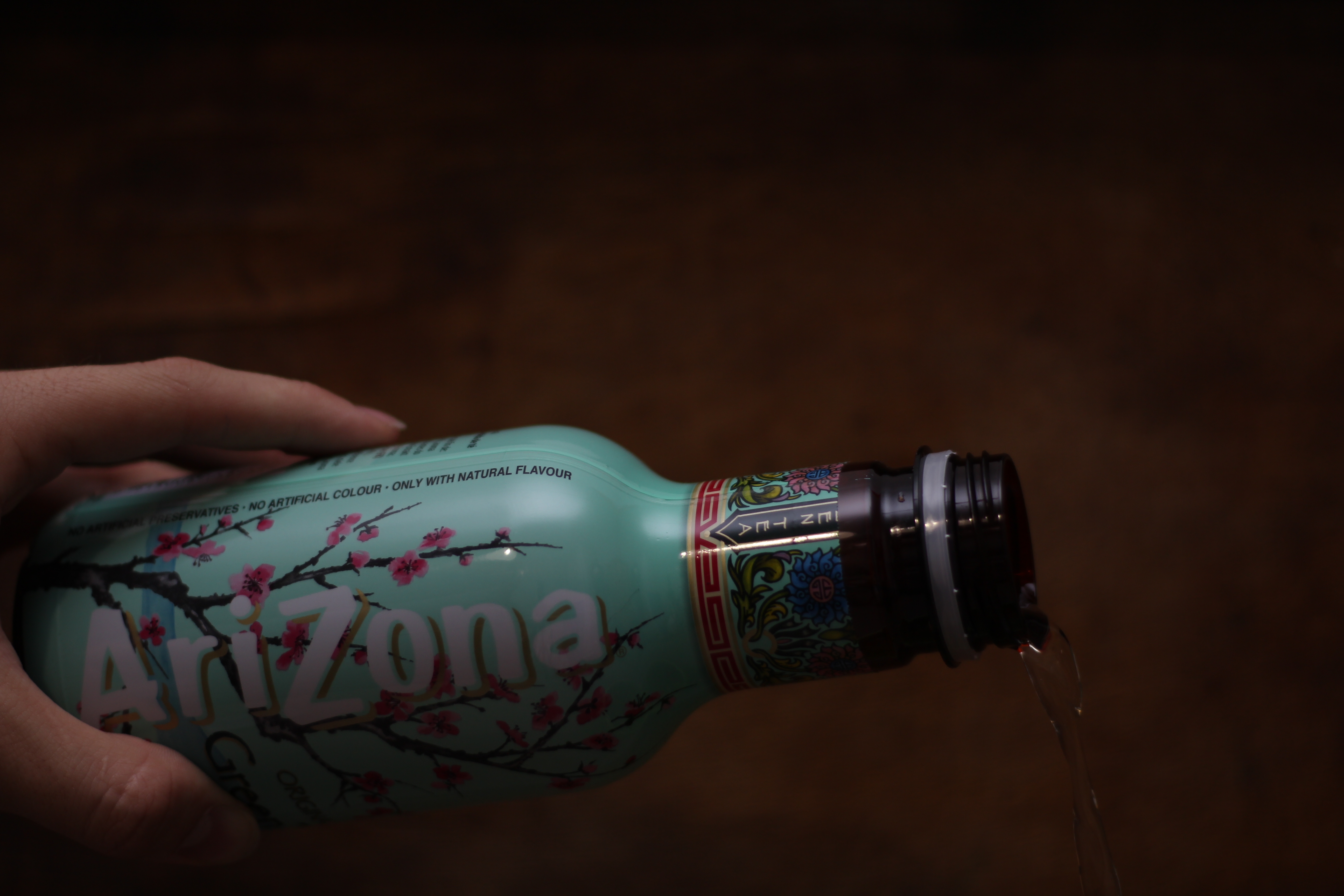 Hand pouring Arizona tea from a patterned bottle