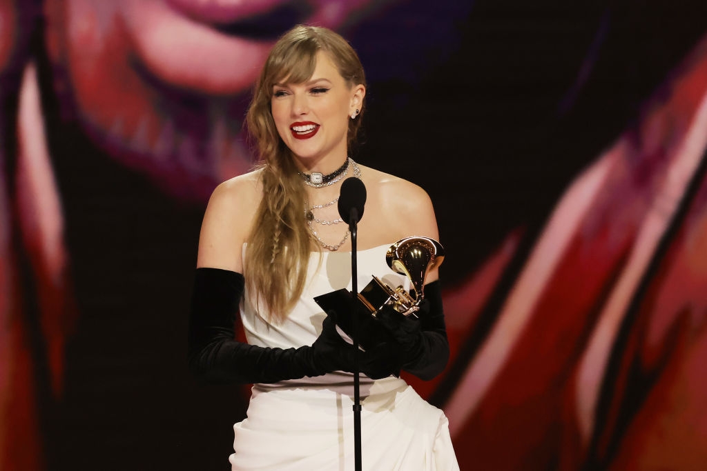 Person wearing a white gown with black gloves, holding a Grammy award on stage