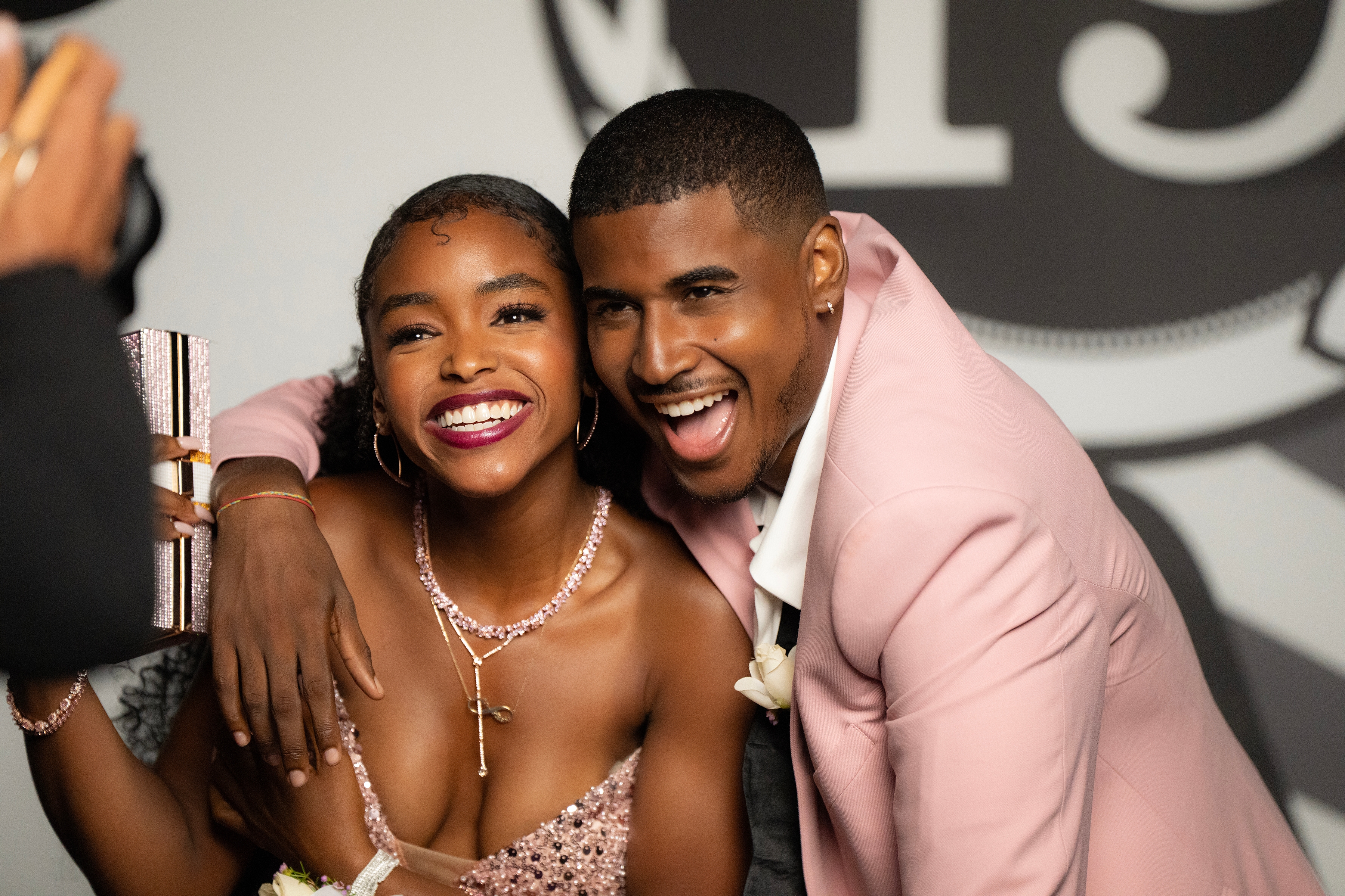 Two people smiling at an event, with the person on the left in a sparkling gown and the person on the right in a light-colored suit