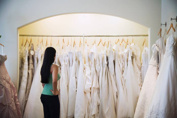 A woman stands in front of a rack of wedding dresses, browsing the selection