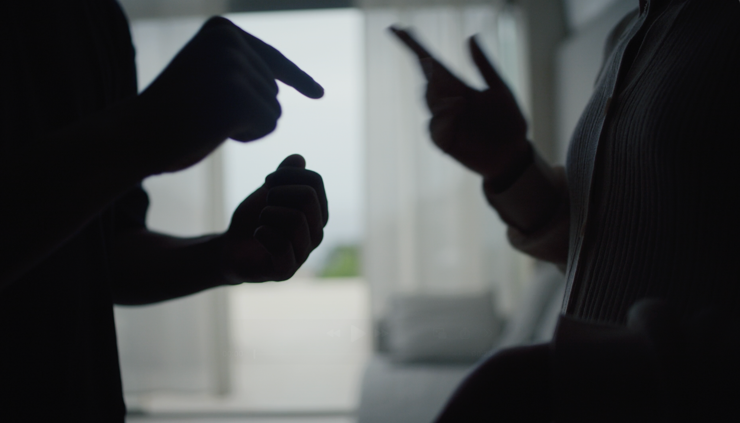 Two people in silhouette are engaged in a conversation using expressive hand gestures in a softly lit indoor setting