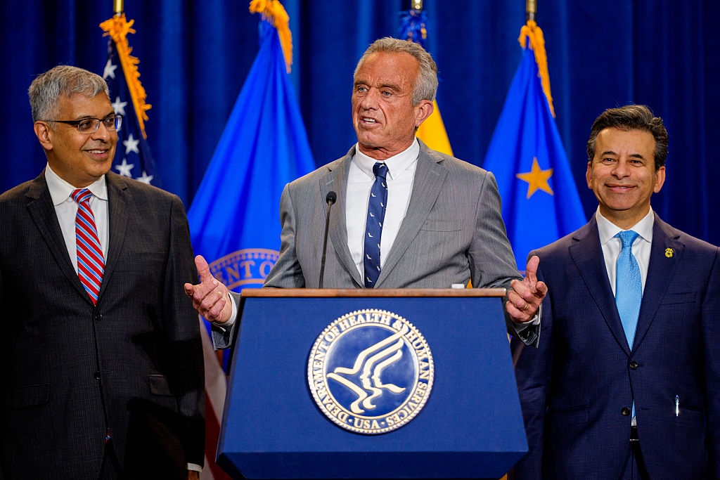 RFK Jr. stands at a podium with National Institutes of Health Director Jayanta Bhattacharya on the left and FDA Commissioner Marty Makary on the right